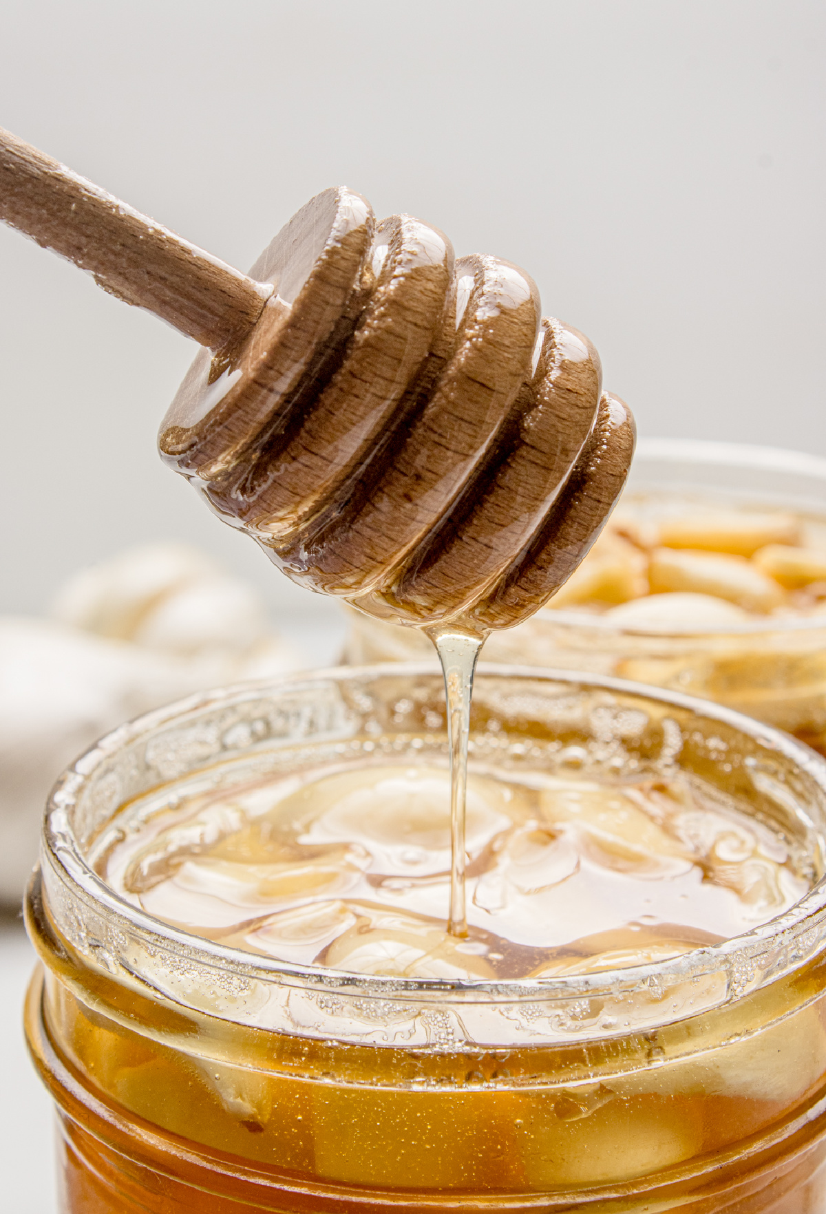 Honey dripping from a wooden honey dipper into a jar of fermented garlic cloves as the honey loosens during fermentation.