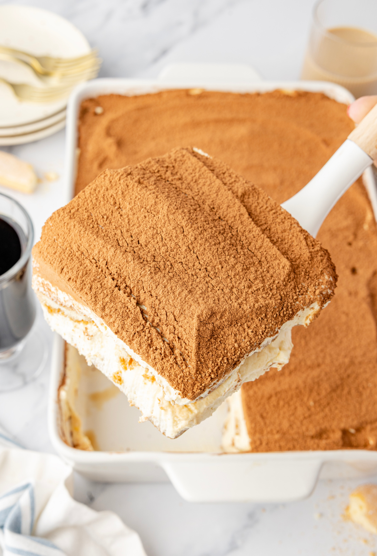 Baileys Irish Cream Tiramisu being lifted from the dish, showing thick layers of mascarpone cream, espresso-soaked ladyfingers, and a cocoa-dusted top.