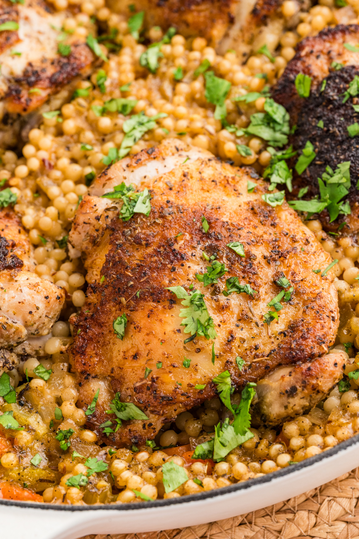 Crispy chicken thighs over pearl couscous baked together in one pan until the skin is golden and the couscous is tender underneath. Crispy chicken thighs over pearl couscous baked in a wide pan with lemon, herbs, and vegetables.