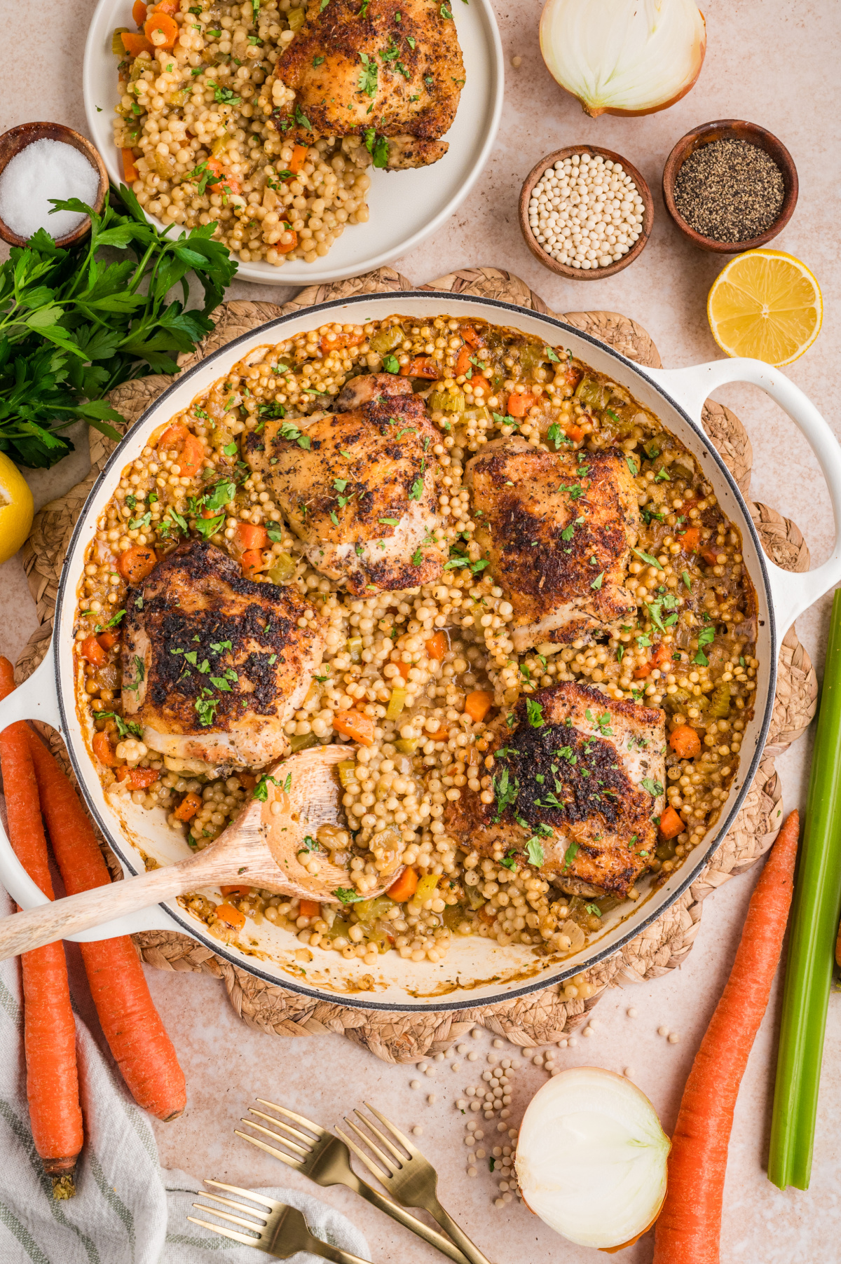 A full pan of crispy chicken thighs over pearl couscous baked together with vegetables and finished with chopped parsley. Crispy chicken thighs over pearl couscous baked in a braiser with carrots, celery, lemon, and herbs.