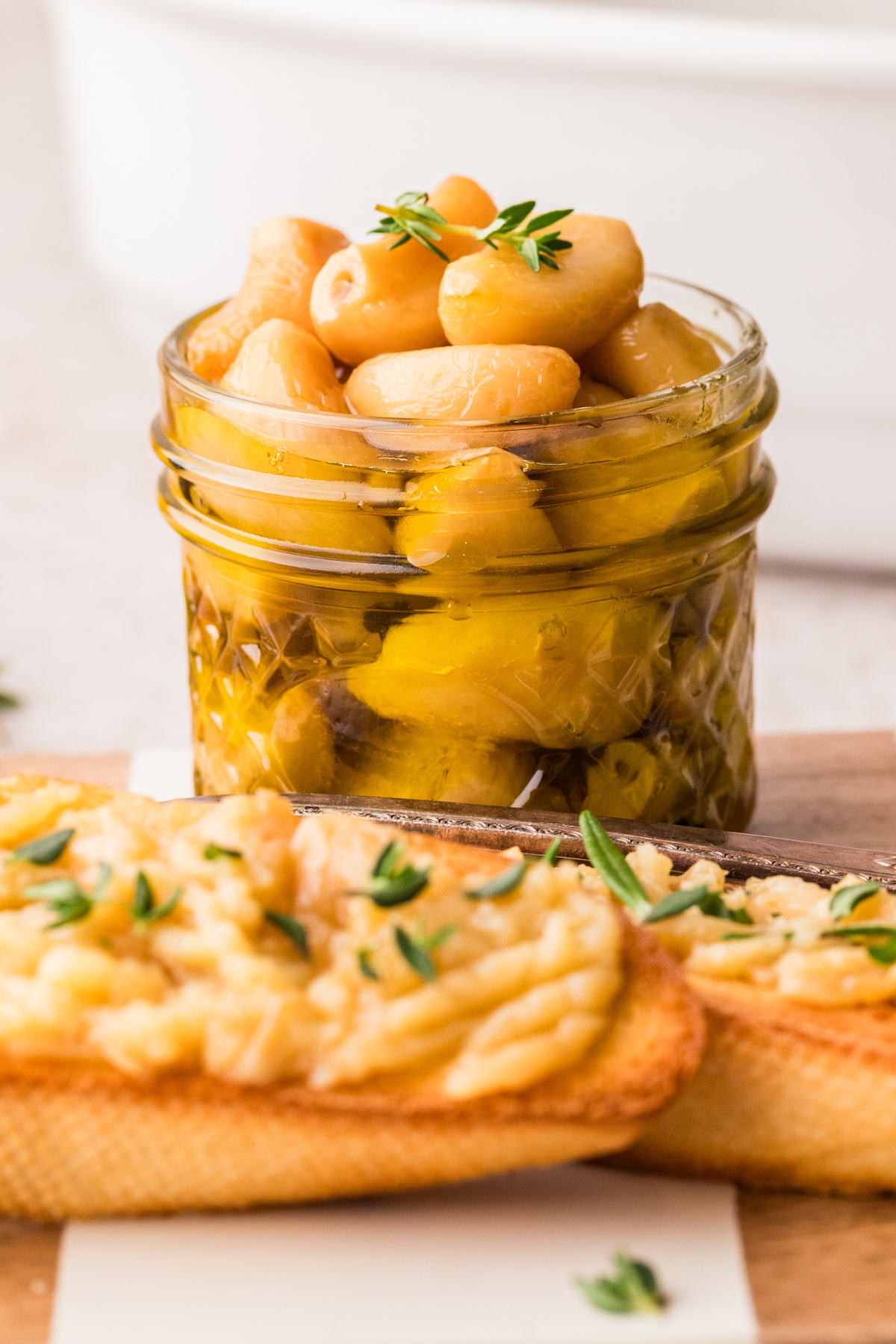 Oven cooking process for garlic cloves gently simmered in olive oil. Step-by-step process showing garlic cloves submerged in olive oil before and after slow cooking in the oven.