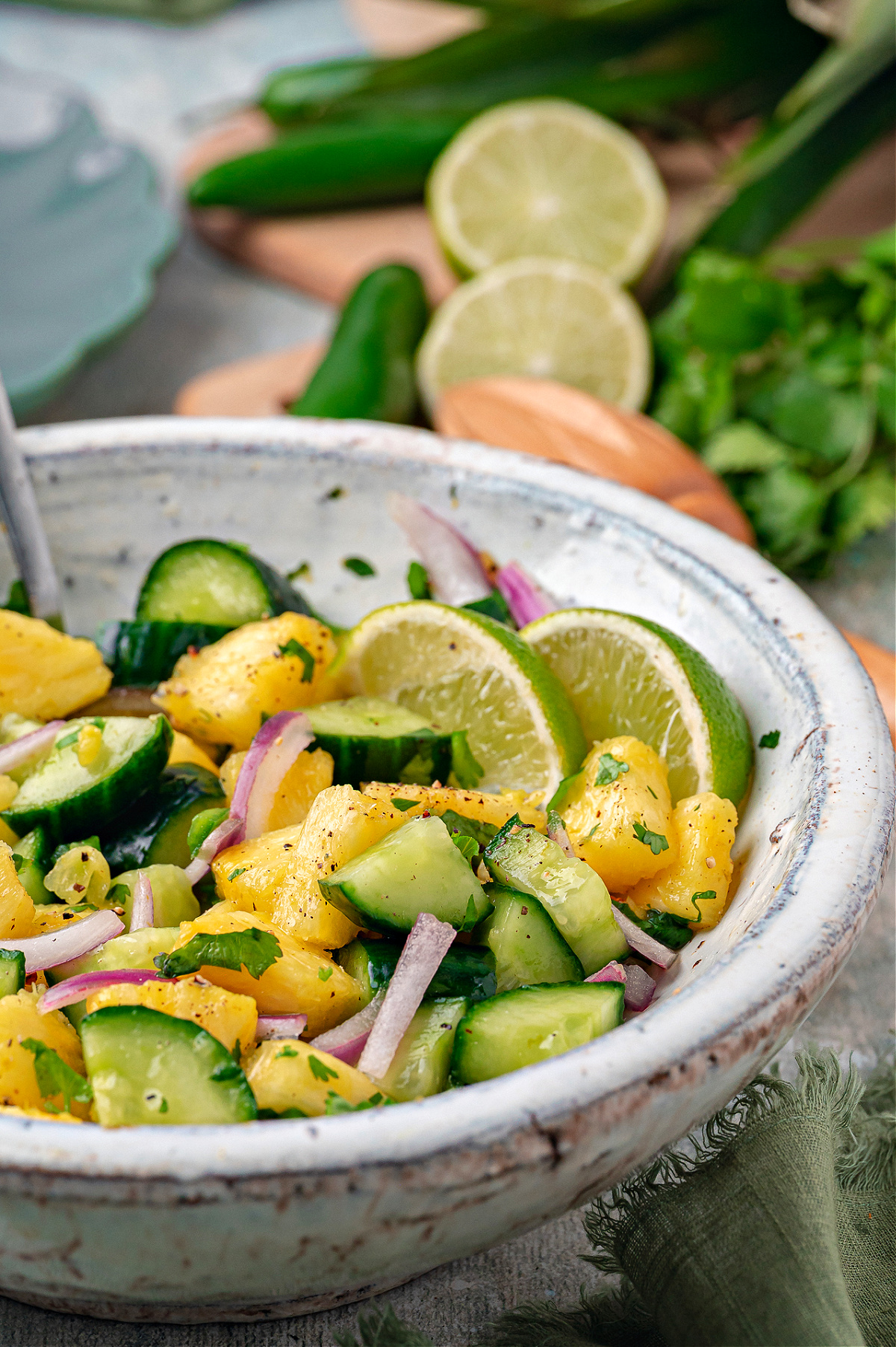 A ceramic bowl filled with chilled pineapple cucumber salad and lime slices. Chilled pineapple cucumber salad with fresh pineapple chunks, sliced cucumber, red onion, cilantro, and lime slices in a ceramic bowl.