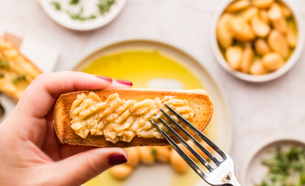 Garlic confit on toast with olive oil and soft spreadable cloves. Garlic confit cloves served on toasted bread, shown close up and ready to eat.