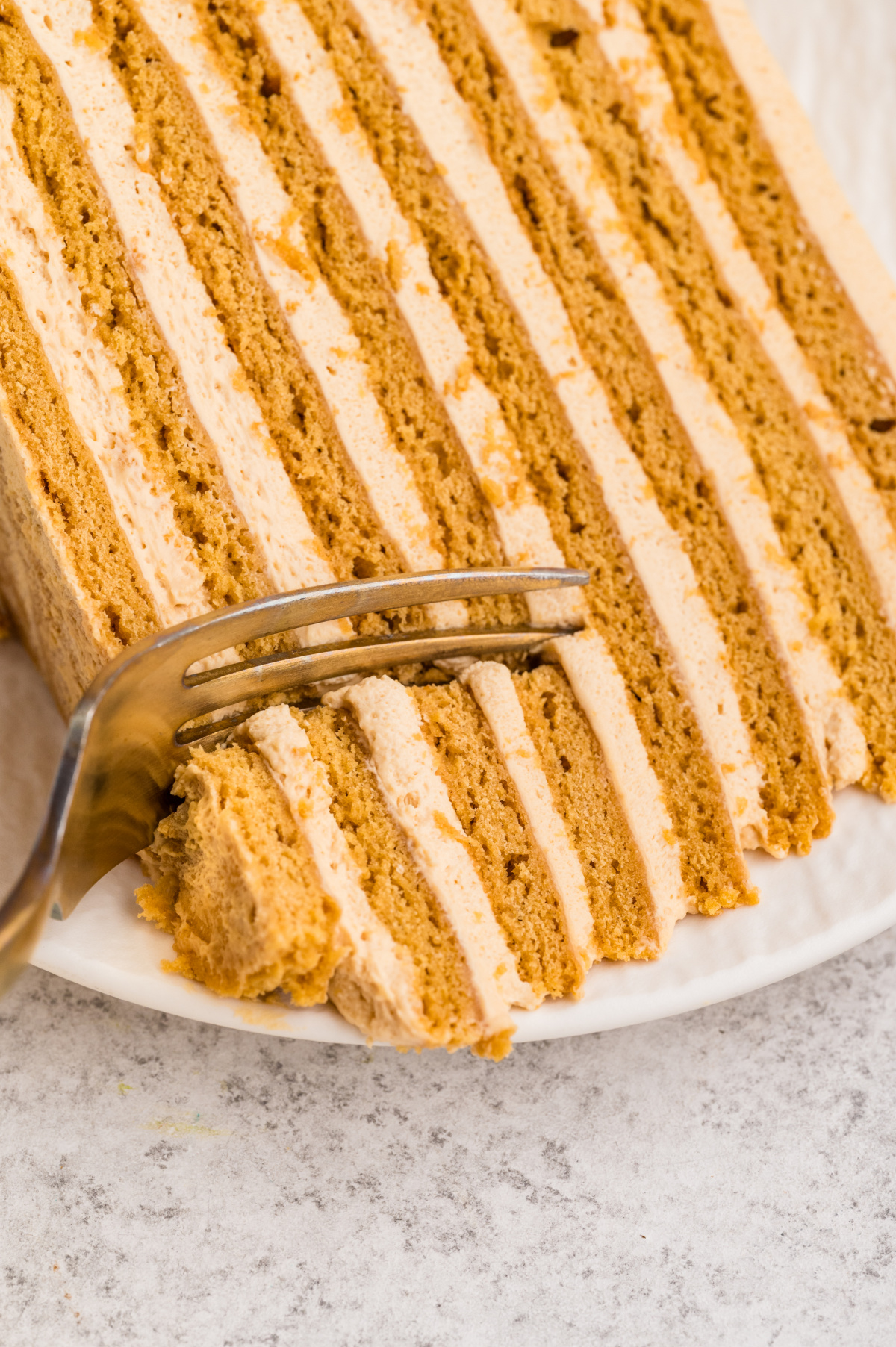 A fork cuts into a slice of Russian honey cake (Medovik), showing soft honey cake layers and creamy dulce de leche frosting.