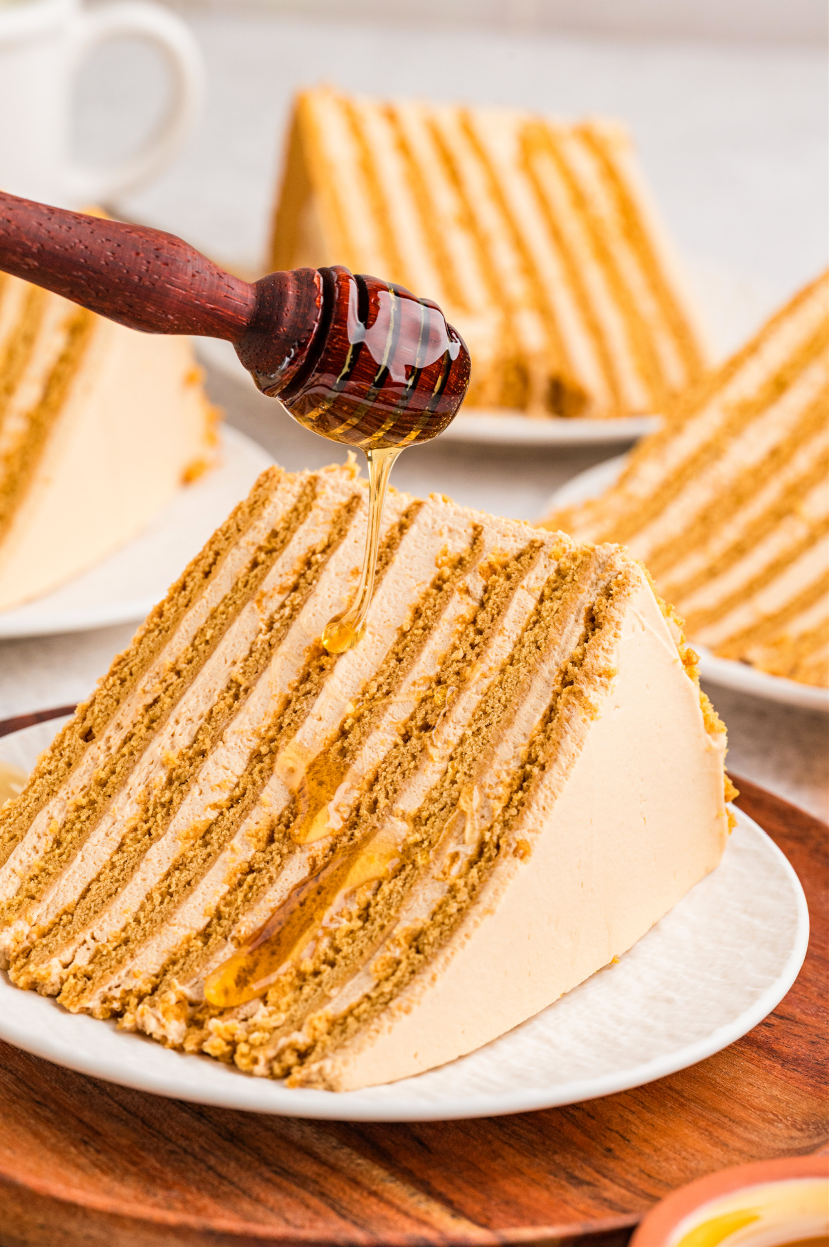 Russian honey cake (Medovik) sliced to show thin baked honey layers with whipped dulce de leche frosting, drizzled with honey.