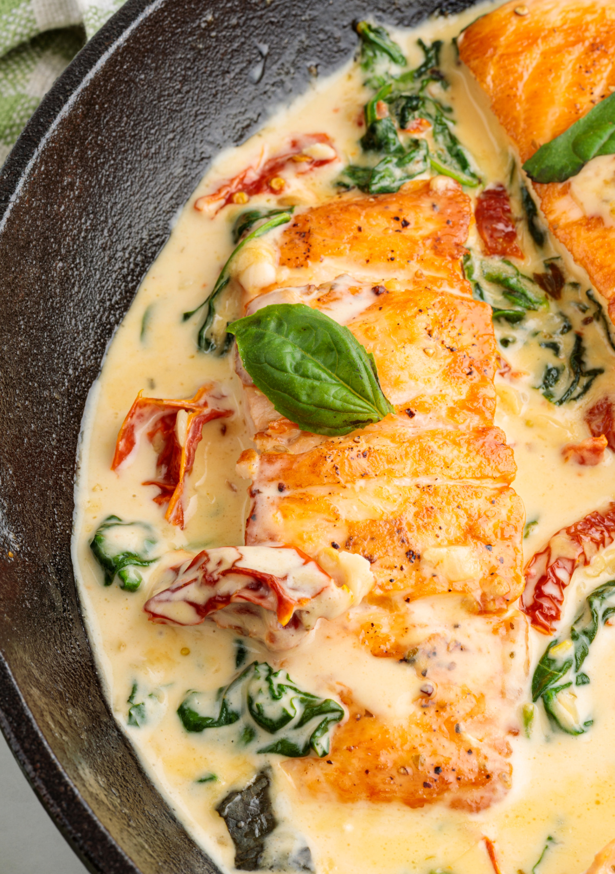 Close-up of salmon fillets finished in a creamy garlic sauce with sun-dried tomatoes and spinach. Marry Me Tuscan salmon simmering in a creamy garlic sauce with sun-dried tomatoes and wilted spinach in a cast iron skillet.