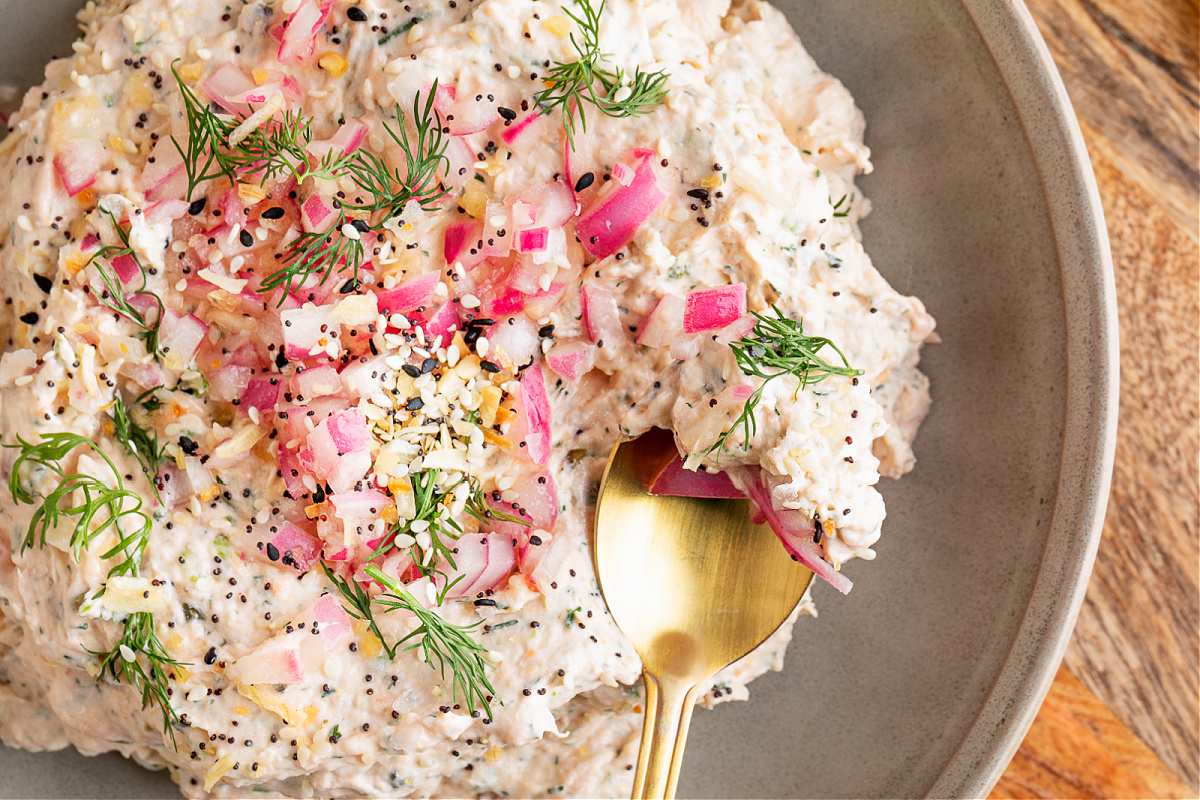 Creamy salmon dip garnished with pickled red onions and dill, styled for serving with bagels or chips. Creamy salmon dip topped with pickled red onions, fresh dill, and everything bagel seasoning, styled on a serving board with lemon halves.
