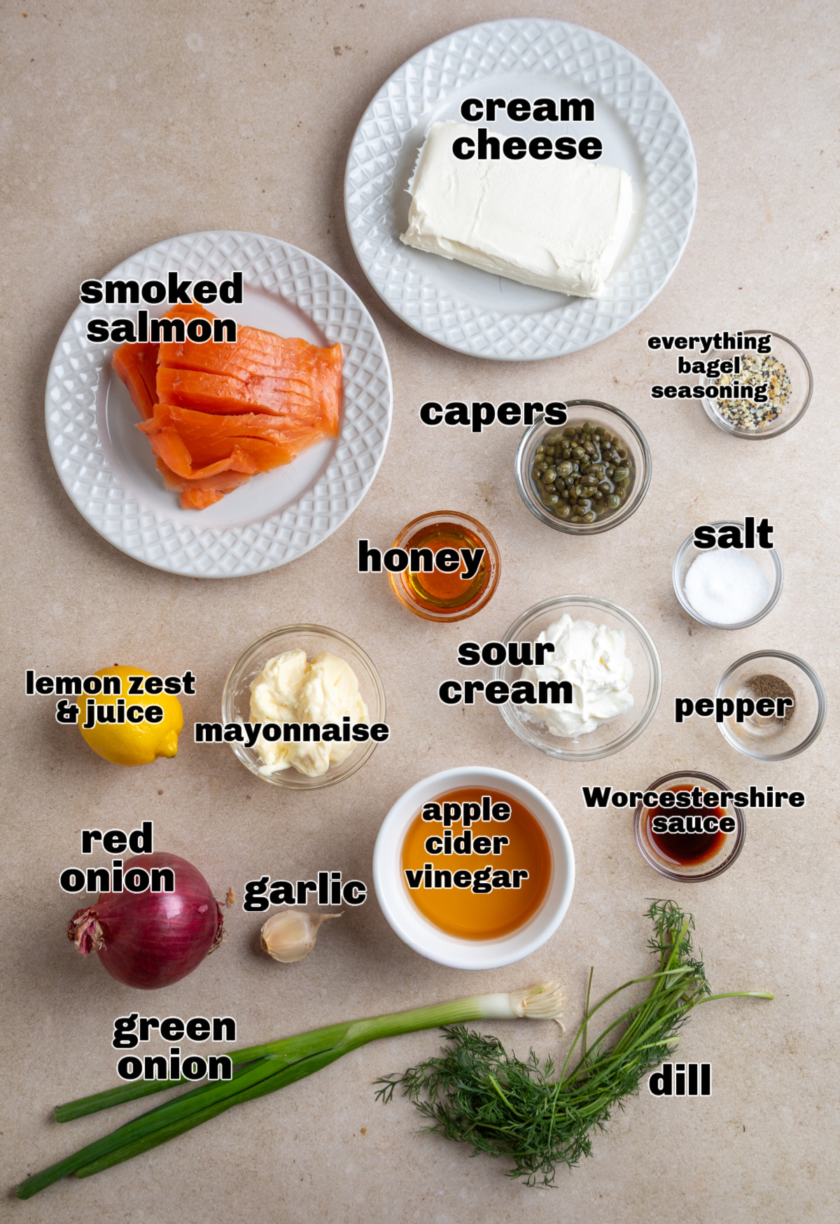 Ingredients laid out for a creamy smoked salmon dip with dill, capers, lemon, and pickled red onion. Ingredients for a smoked salmon cream cheese dip arranged on a light surface, including smoked salmon, cream cheese, sour cream, capers, dill, lemon, and red onion.