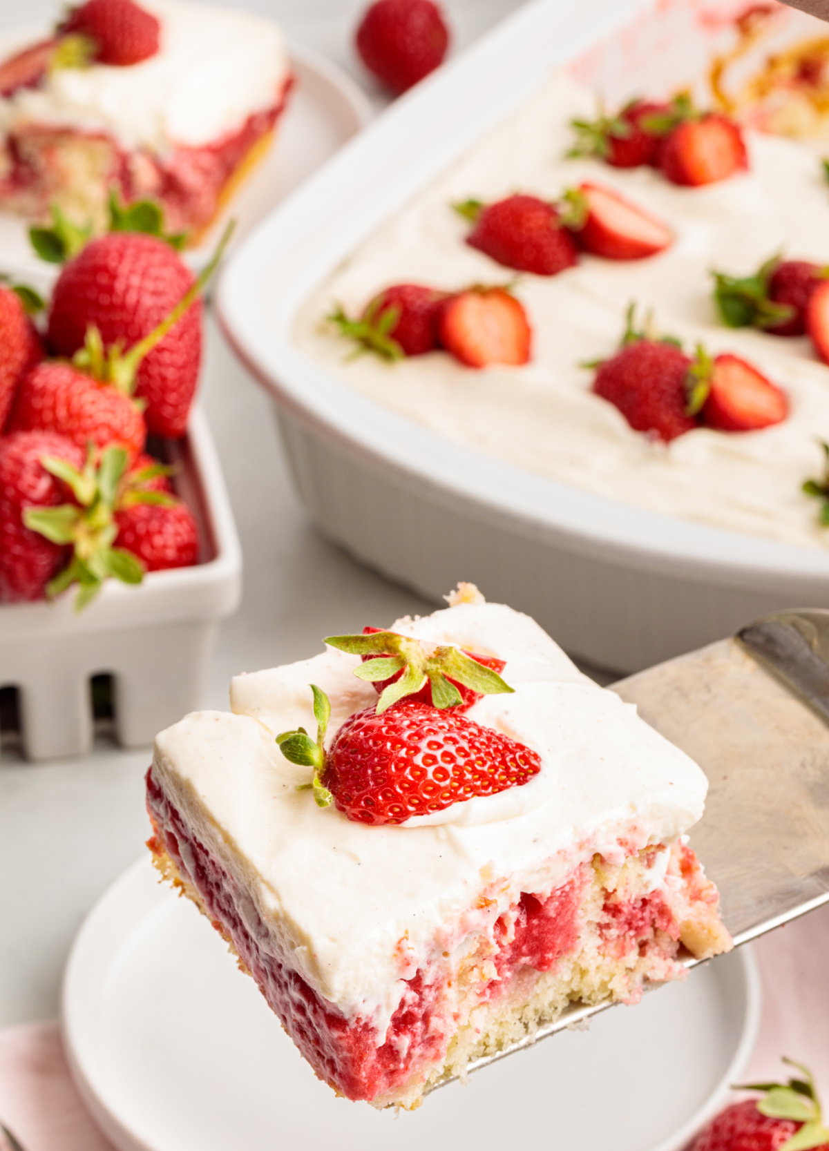 This slice of strawberry cake made from white cake mix shows the soaked strawberry filling and whipped vanilla cream cheese frosting as it’s lifted from the pan. Slice of strawberry cake made from white cake mix with a soaked strawberry filling and whipped vanilla cream cheese frosting, lifted from the pan on a metal spatula.