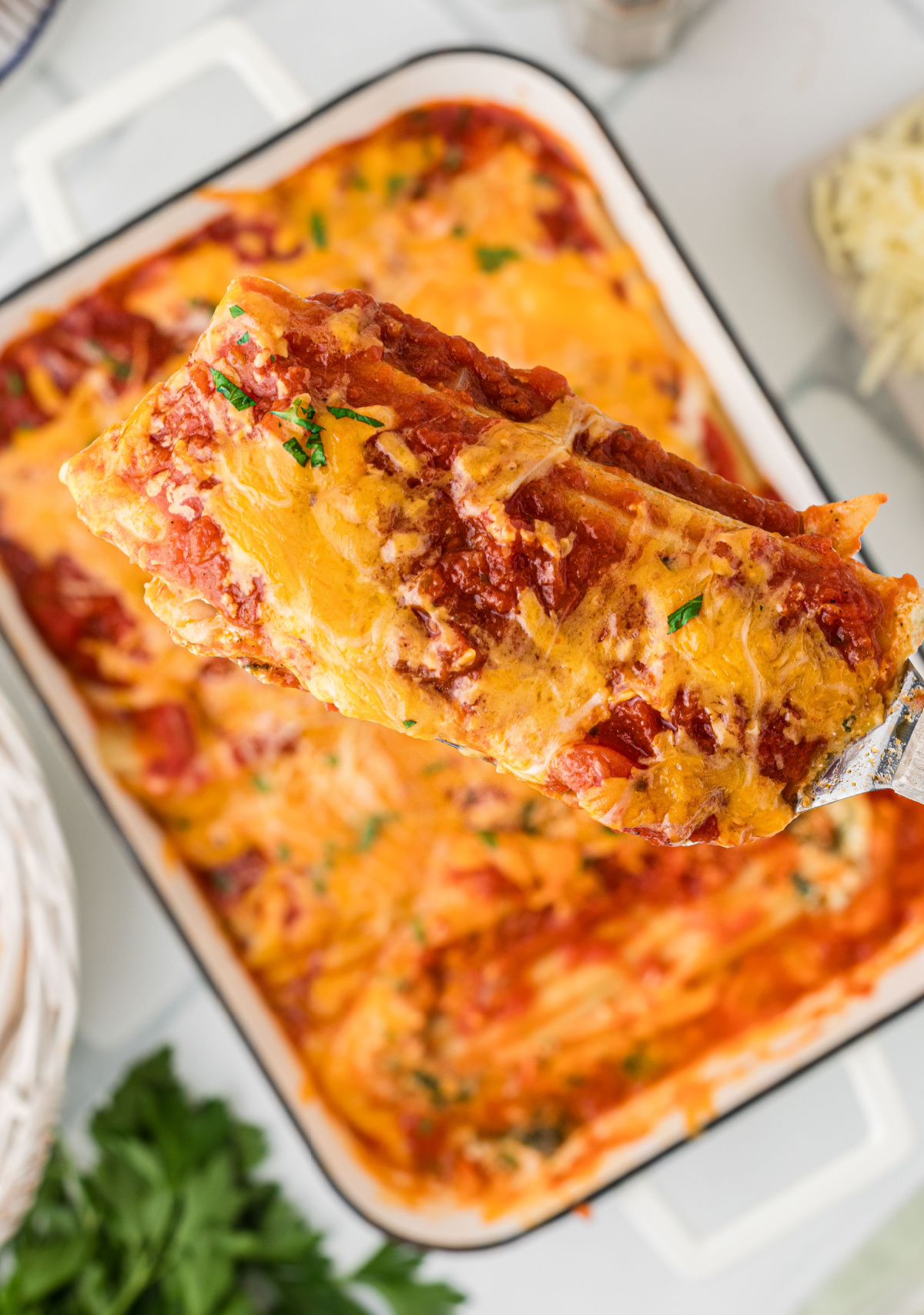 Stuffed manicotti shell lifted from the pan with ricotta spinach filling, marinara sauce, and melted cheddar cheese