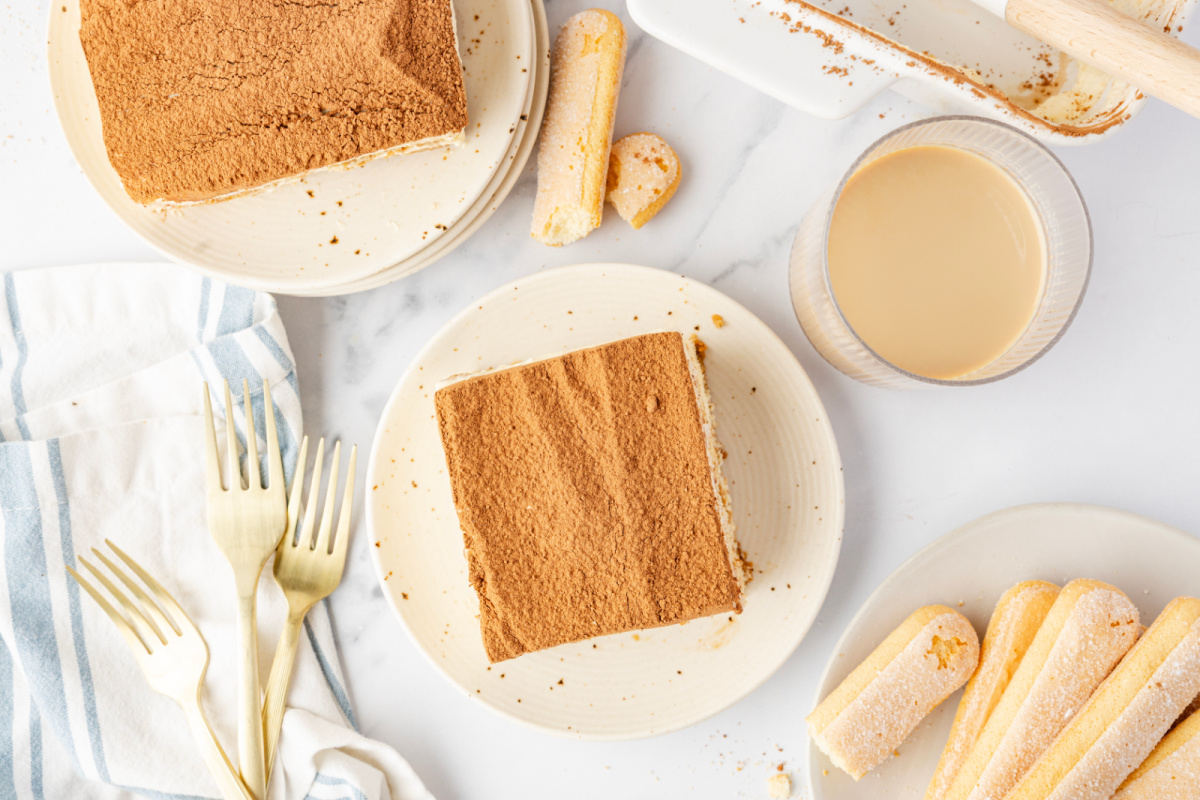 Overhead view of plated tiramisu squares dusted with cocoa powder, with ladyfingers and a glass of Irish cream coffee on the side.
