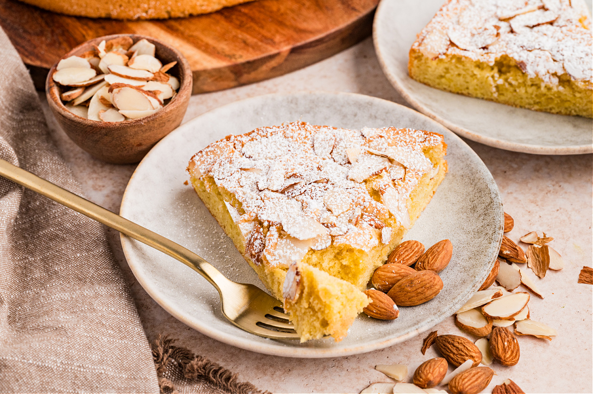 Almond cake slice with a forkful taken out, showing the soft interior and sliced almonds on top