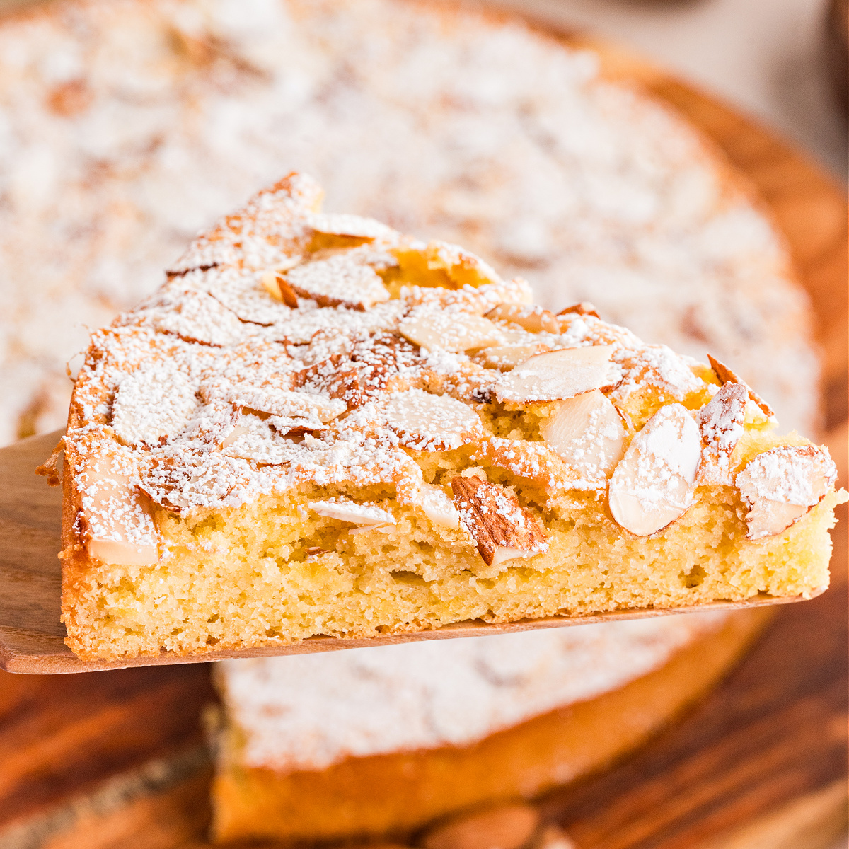Almond cake topped with sliced almonds and powdered sugar, showing the soft interior and golden crumb