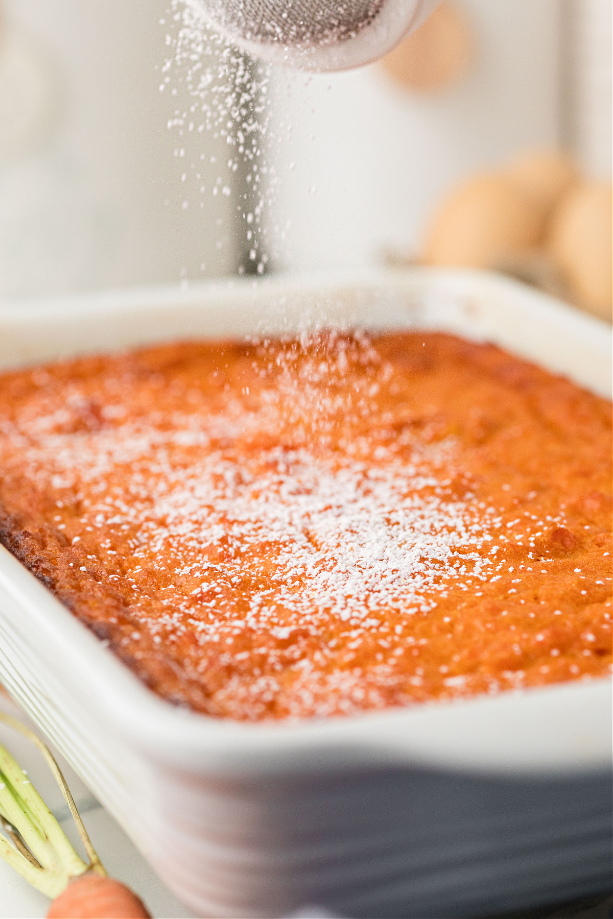 Carrot Souffle dusted with powdered sugar in baking dish Baked carrot casserole with powdered sugar in white 11x7 baking dish