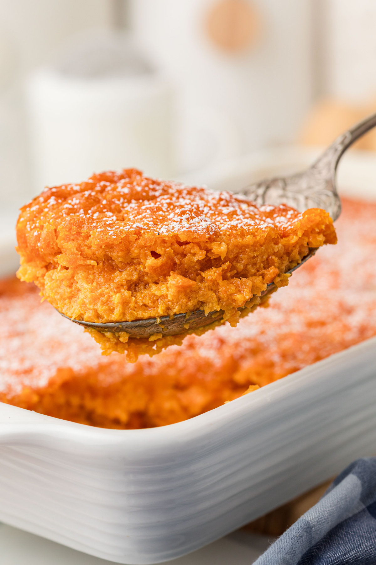 Carrot Souffle served on spoon from casserole dish Spoon lifting a serving of Carrot Souffle from white baking dish
