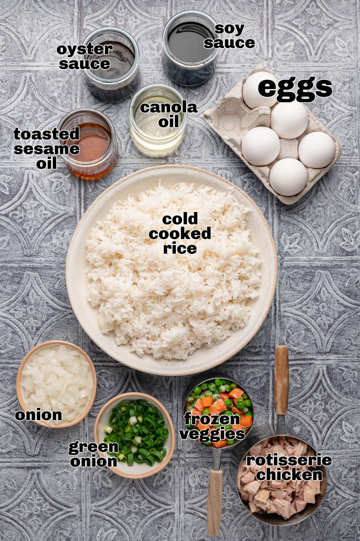Overhead layout of chicken fried rice ingredients with cold cooked rice, rotisserie chicken, eggs, onion, green onions, frozen vegetables, soy sauce, oyster sauce, toasted sesame oil, and canola oil Chicken fried rice ingredients including cold cooked rice, rotisserie chicken, eggs, soy sauce, oyster sauce, and vegetables