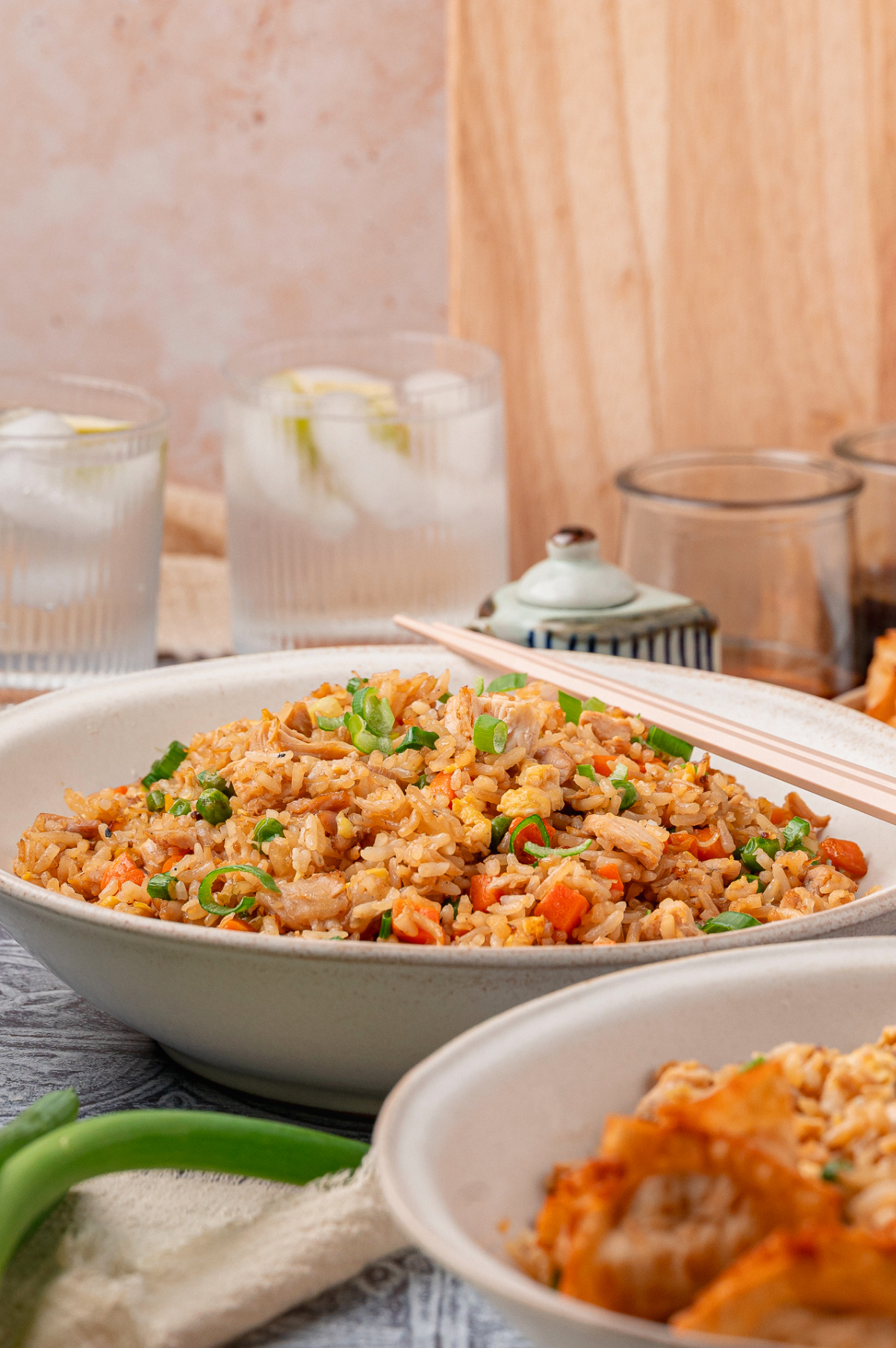 Side view of fried rice made with leftover chicken, scrambled eggs, peas, carrots, and sliced green onions, served in a shallow bowl with chopsticks nearby Homemade fried rice with chicken, eggs, peas, carrots, and green onions served in a wide bowl