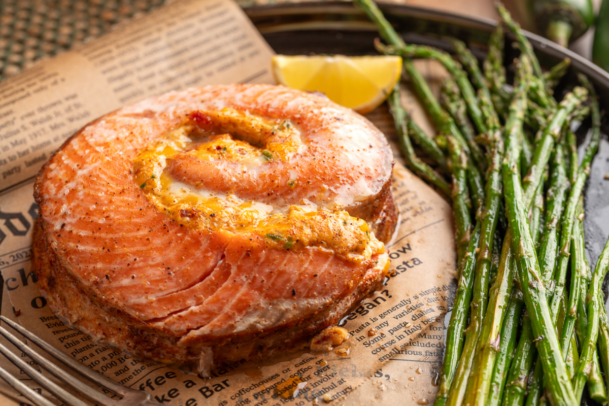 Close-up of a thick baked salmon pinwheel showing the creamy jalapeño popper-style filling, served with roasted asparagus and lemon. Baked stuffed salmon pinwheel with creamy jalapeño popper filling and roasted asparagus