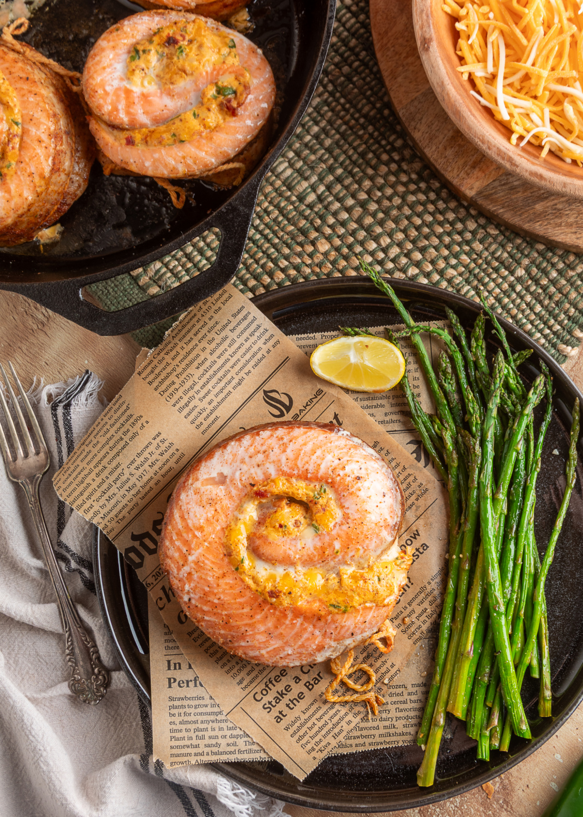 Finished baked salmon rolls with a jalapeño popper-style filling, shown both in the cast iron skillet and plated with roasted asparagus and lemon. Chipotle jalapeño popper stuffed salmon rolls baked in a cast iron skillet and plated for serving