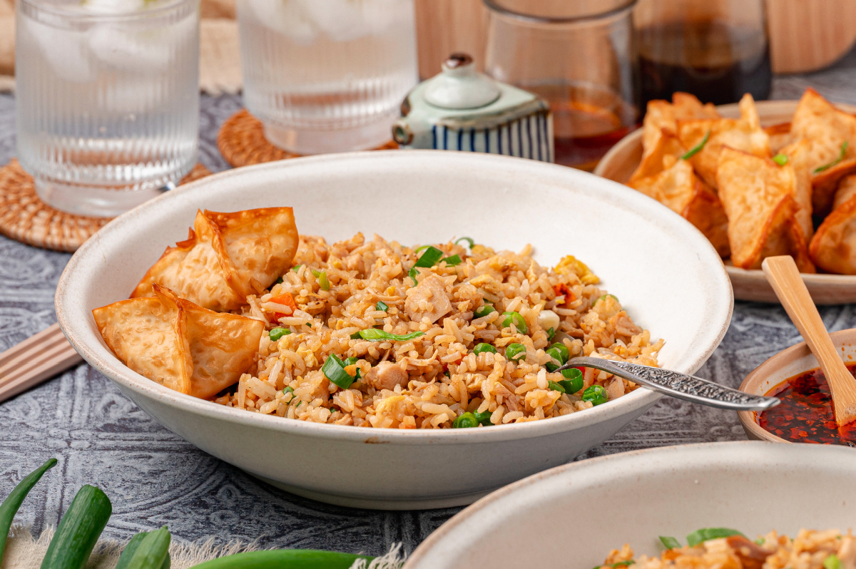 Bowl of chicken fried rice made with cold cooked rice, rotisserie chicken, scrambled eggs, peas, carrots, and sliced green onions, served with crispy wontons on the side Chicken fried rice served in a bowl with crispy wontons and green onions