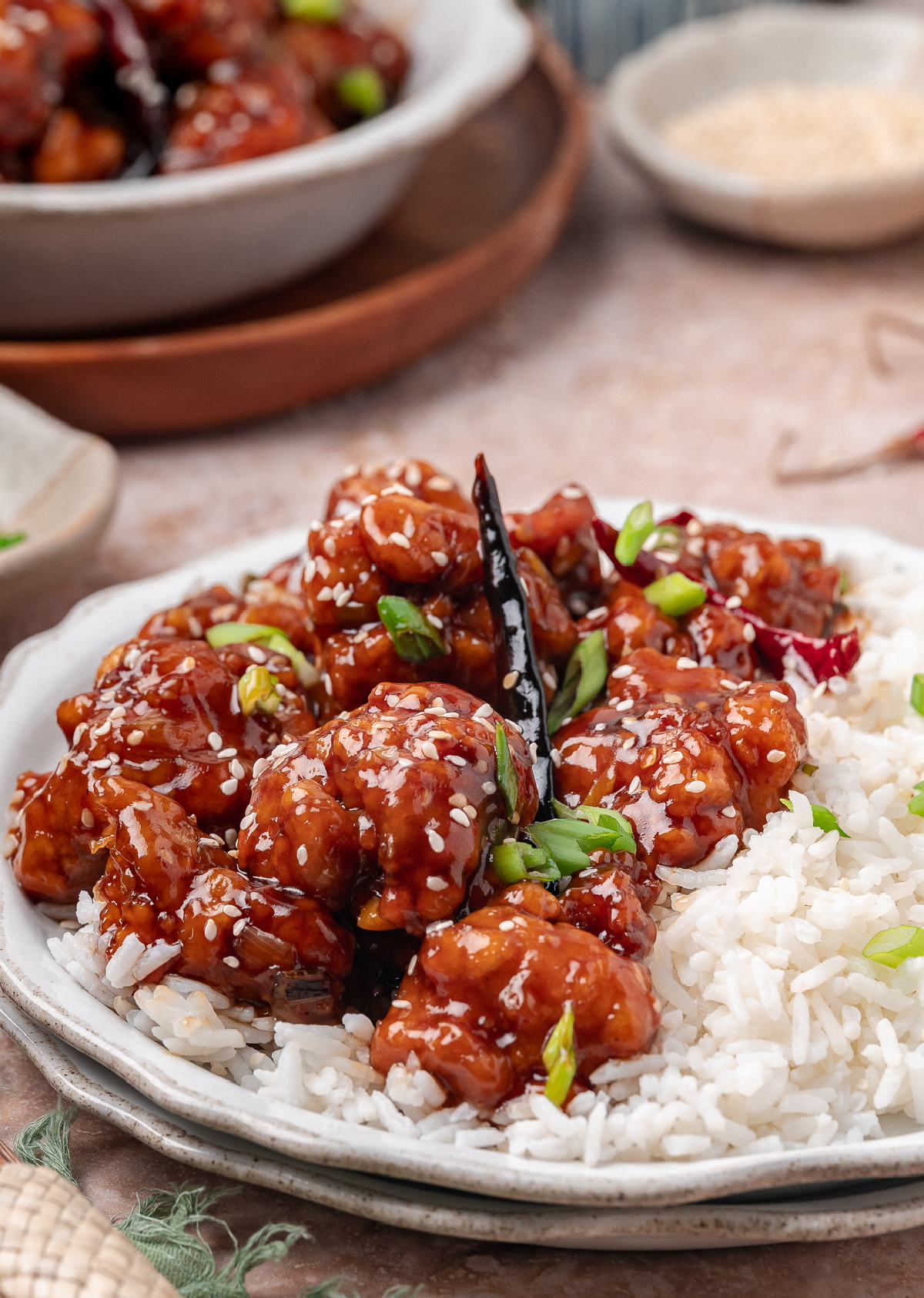 A plated serving of crispy sauced chicken over steamed rice with green onions and sesame seeds Crispy Chinese-American chicken served over steamed rice with scallions and sesame seeds