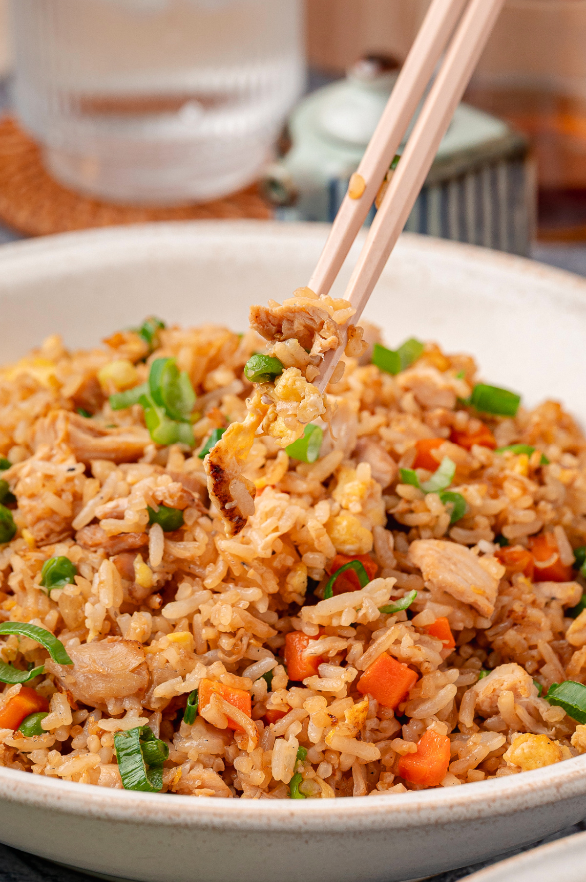 Close-up of fried rice made with cold cooked rice, rotisserie chicken, scrambled eggs, mixed vegetables, and sliced green onions, lifted with chopsticks Chicken fried rice with rotisserie chicken, eggs, vegetables, and green onions in a bowl