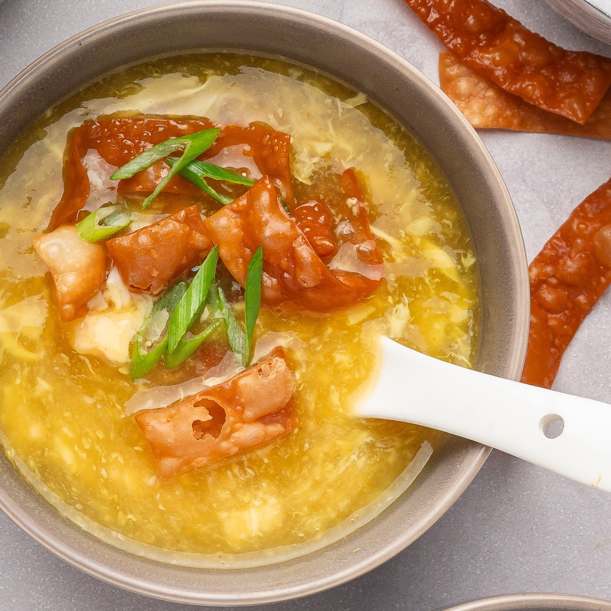 Egg drop soup with crispy fried wonton strips and scallions in a gray bowl