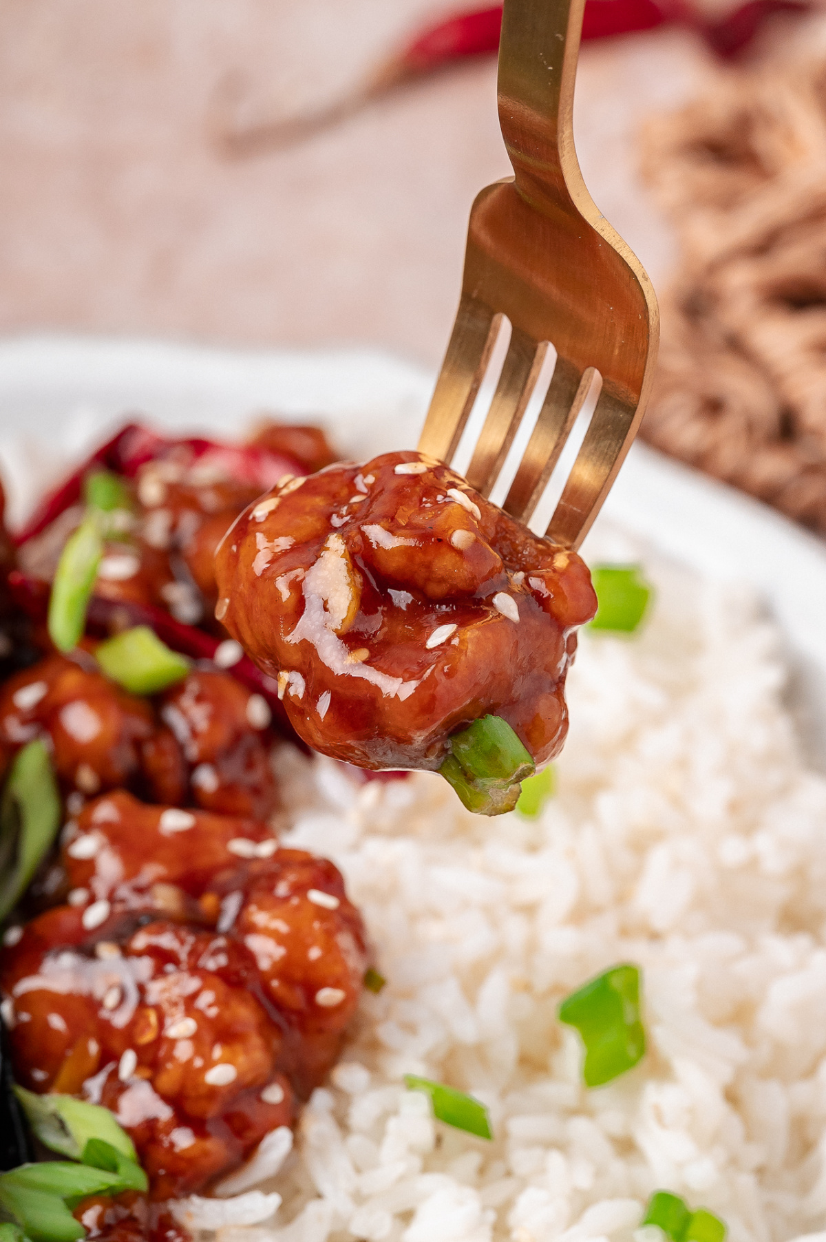 Sauced chicken bite lifted on a fork showing glossy coating and tender interior Close-up of glazed fried chicken piece on a fork over white rice with sesame seeds and scallions