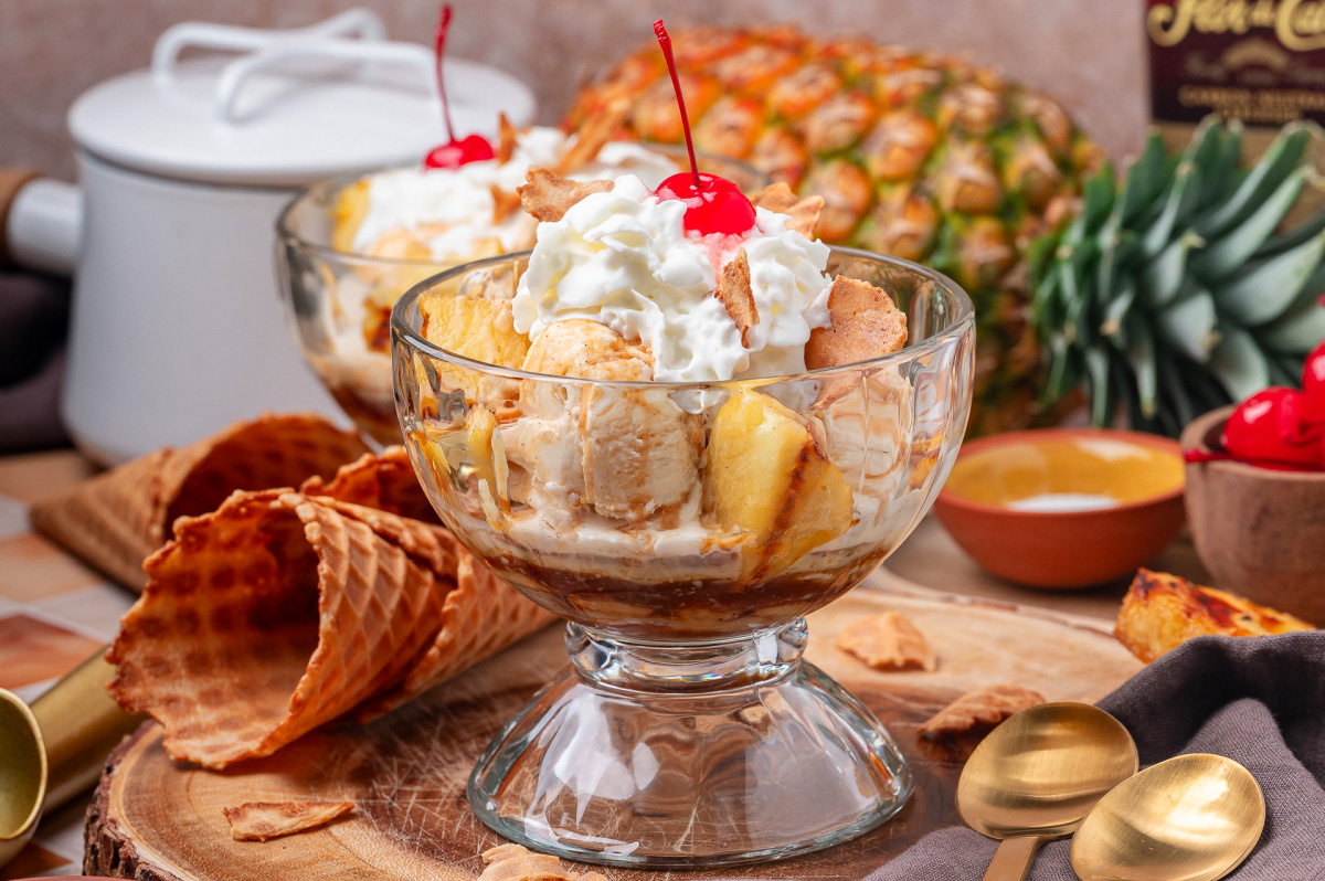 Grilled pineapple sundae with rum sauce, vanilla ice cream, and whipped cream served in a glass bowl Grilled pineapple sundae with rum sauce, vanilla ice cream, and whipped cream served in a glass bowl