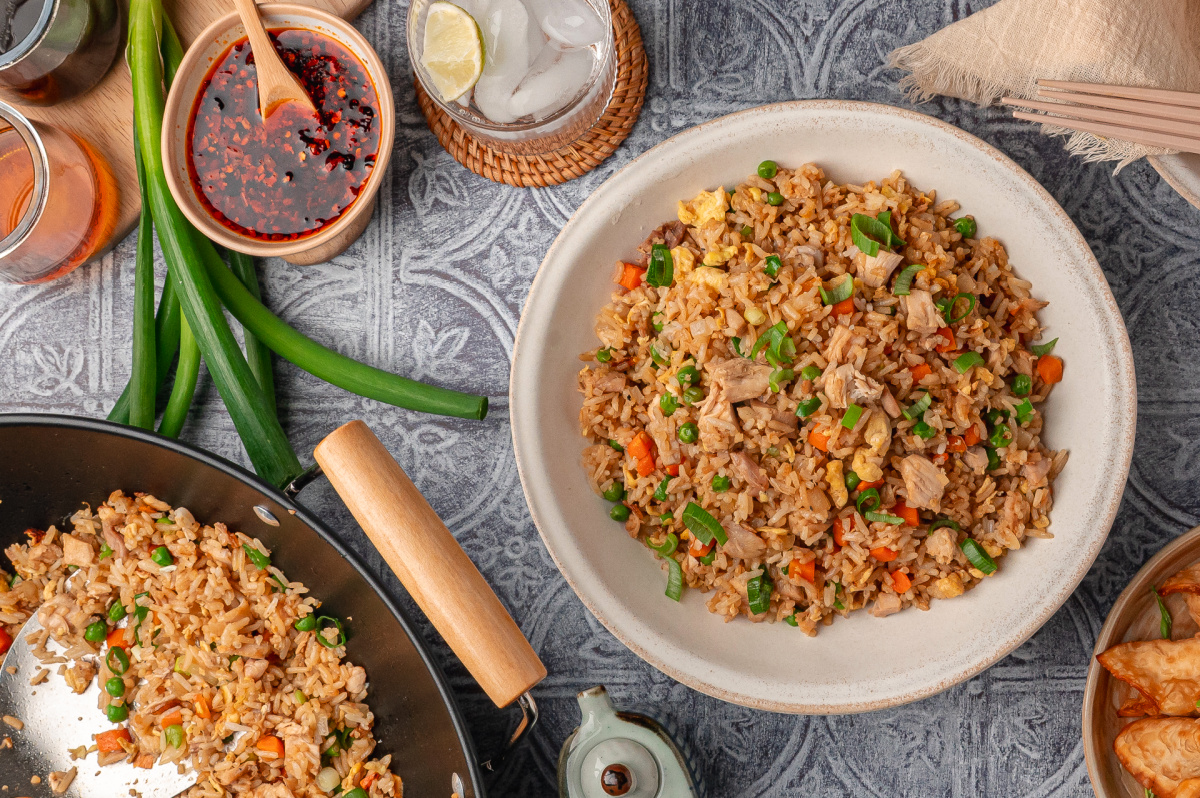erhead view of chicken fried rice made with cold cooked rice, rotisserie chicken, scrambled eggs, mixed vegetables, and green onions, with the wok and serving bowl on the table Chicken fried rice with rotisserie chicken, vegetables, and green onions served from a wok and bowl