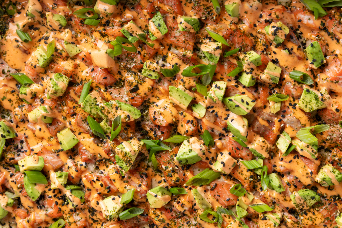 Close-up of Salmon Crab Sushi Bake topped with spicy mayo, avocado, green onions, and black sesame seeds