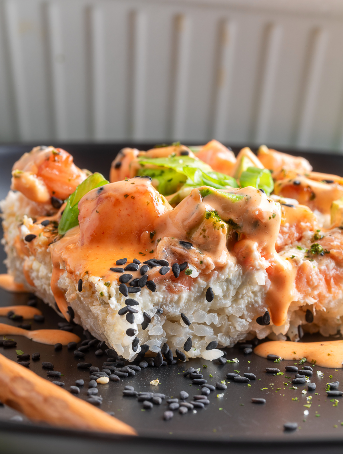 Salmon Crab Sushi Bake slice with spicy mayo, sesame seeds, and green onions on a dark plate