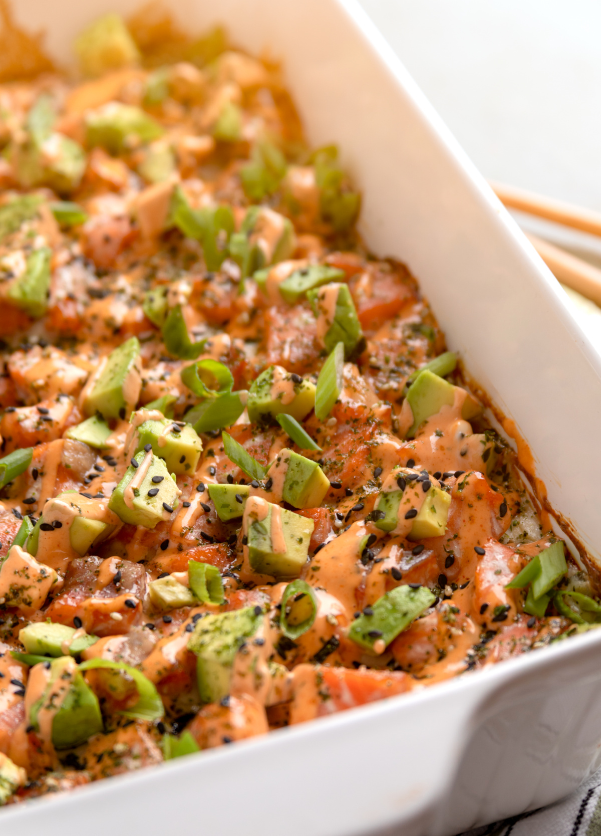 Salmon Crab Sushi Bake baked in a 9x13 dish topped with spicy mayo, avocado, and green onions