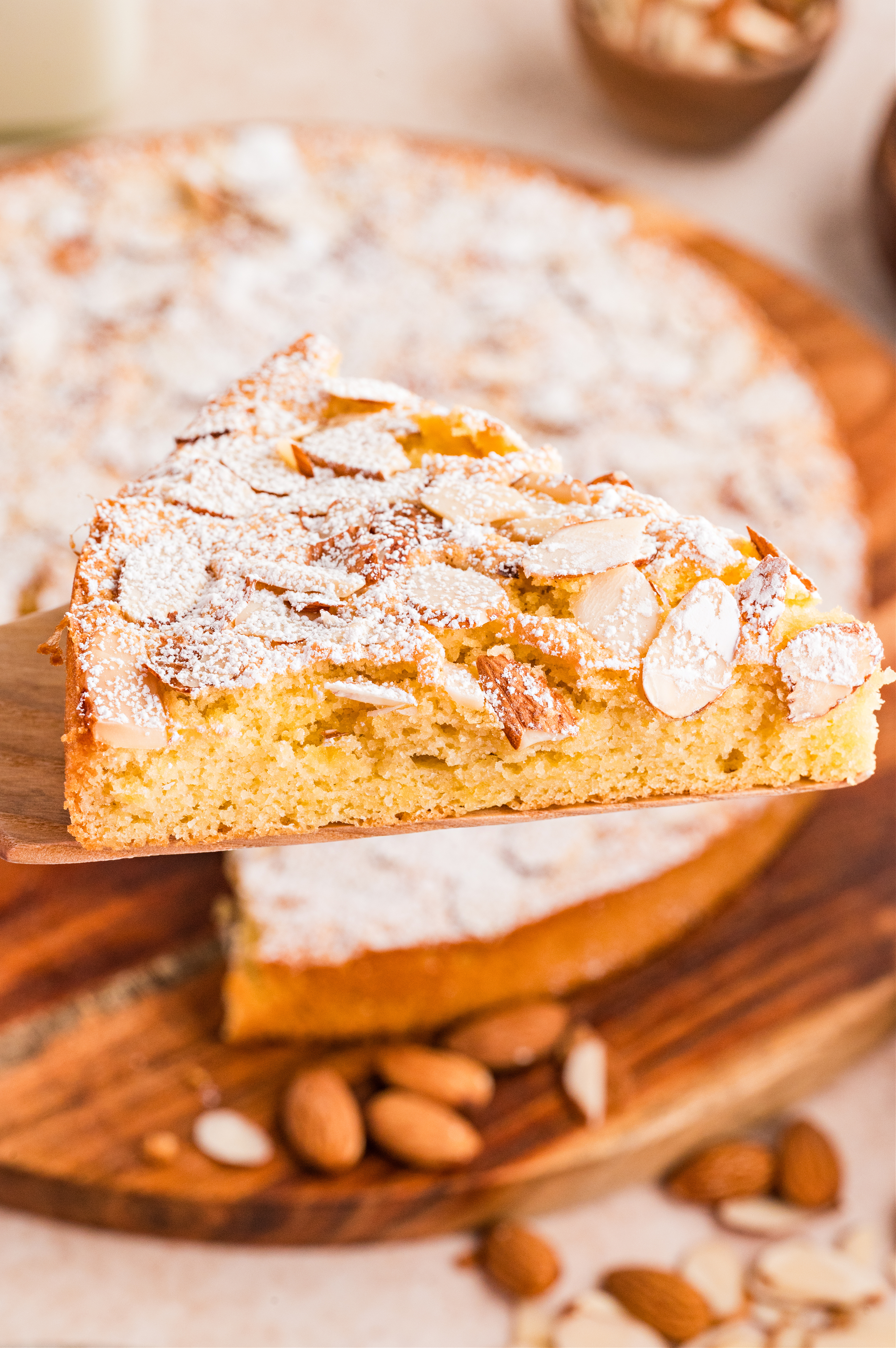 Slice of almond cake with sliced almonds and powdered sugar on top, showing the light, tender crumb