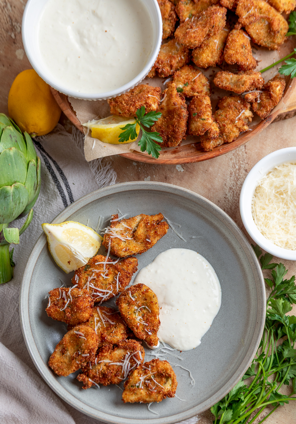 Breaded artichokes with creamy lemon garlic aioli and Parmesan Breaded artichoke hearts with lemon garlic aioli served on plates with lemon wedges and Parmesan