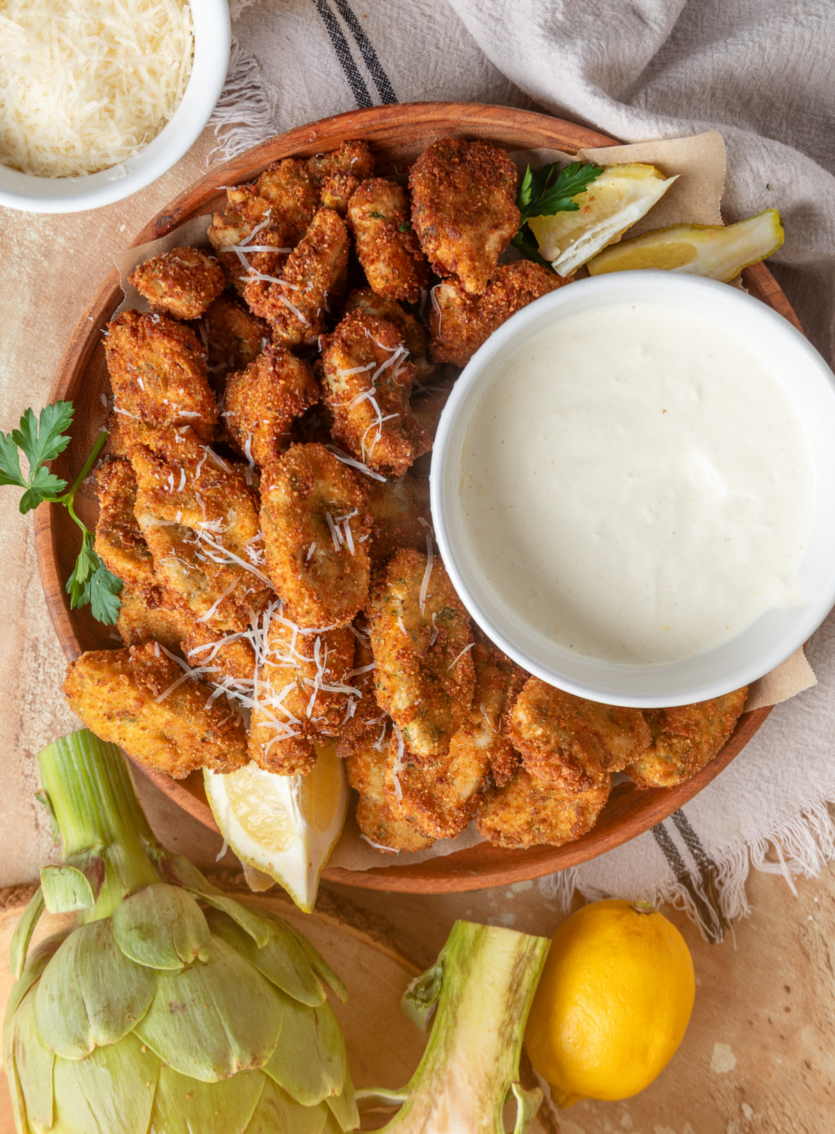 Breaded artichokes with lemon garlic aioli and fresh lemon wedges Breaded artichoke hearts served with lemon garlic aioli, lemon wedges, and Parmesan on a wooden platter
