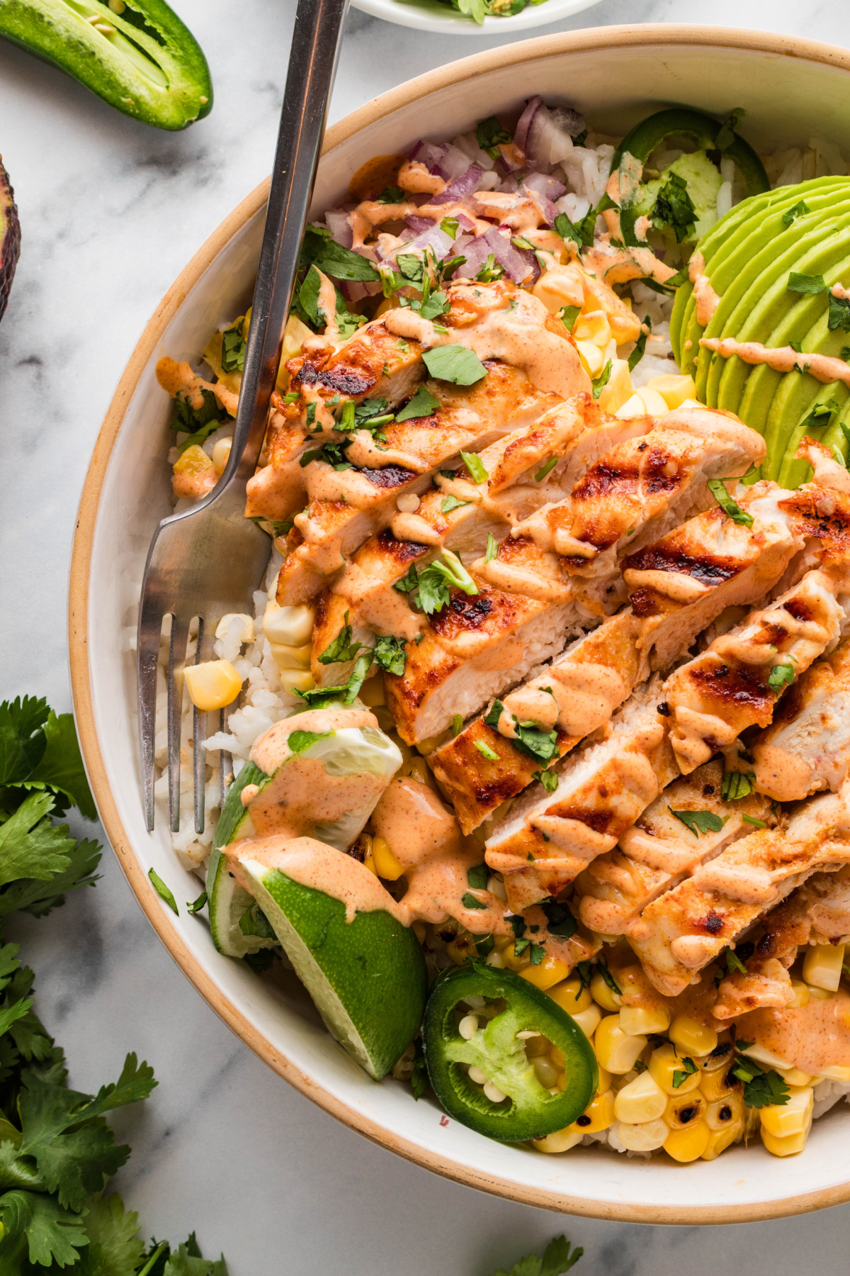 chicken rice bowl with corn, avocado, and lime crema drizzle grilled chicken rice bowl with charred corn, avocado, lime wedge, jalapeños, and creamy elote-style sauce