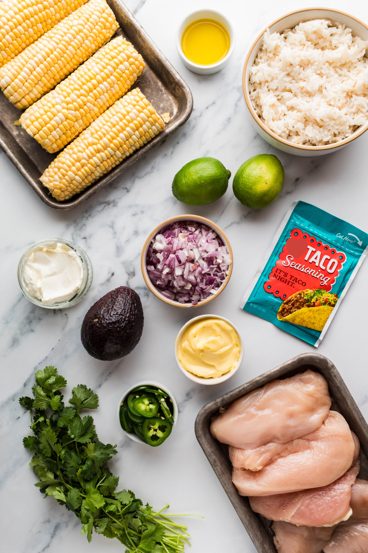 ingredients for grilled chicken rice bowls with corn and lime ingredients for chicken rice bowls including corn, rice, chicken breasts, avocado, lime, red onion, jalapeños, mayonnaise, and taco seasoning