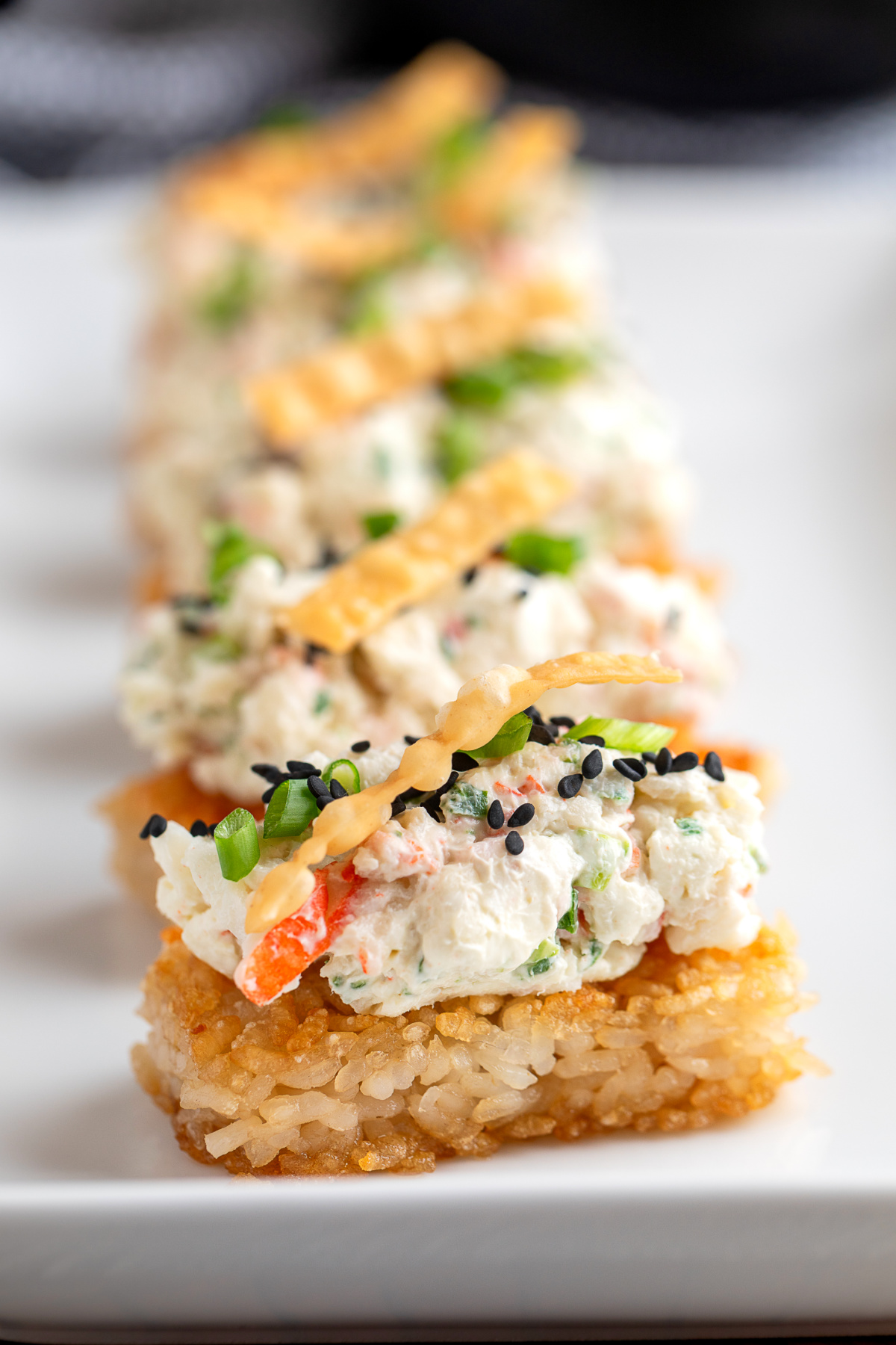 Crispy Rice Crab Rangoon Bites with creamy crab topping, green onions, sesame seeds, and wonton strips