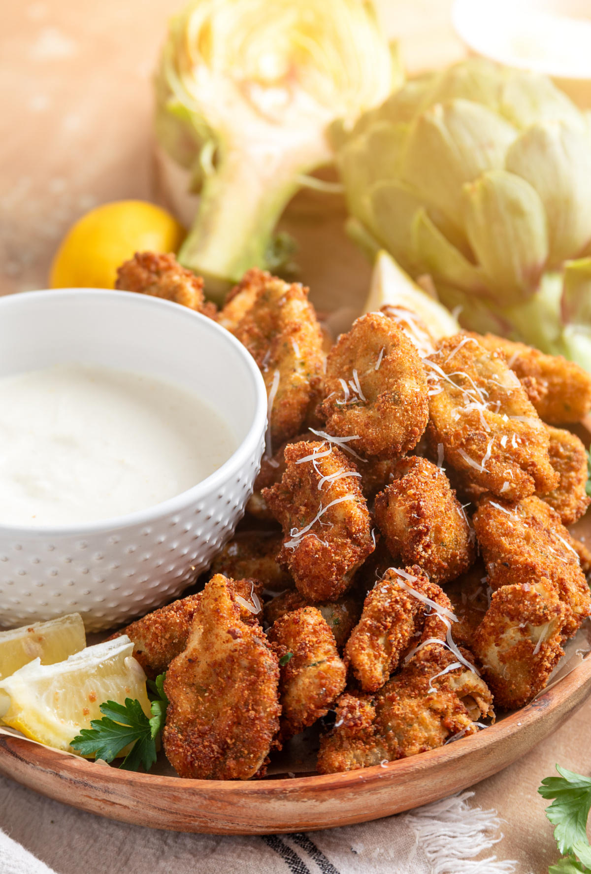 Crispy fried artichokes with lemon garlic aioli and fresh lemon wedges Fried artichokes with lemon garlic aioli served on a wooden platter with lemon wedges and grated Parmesan