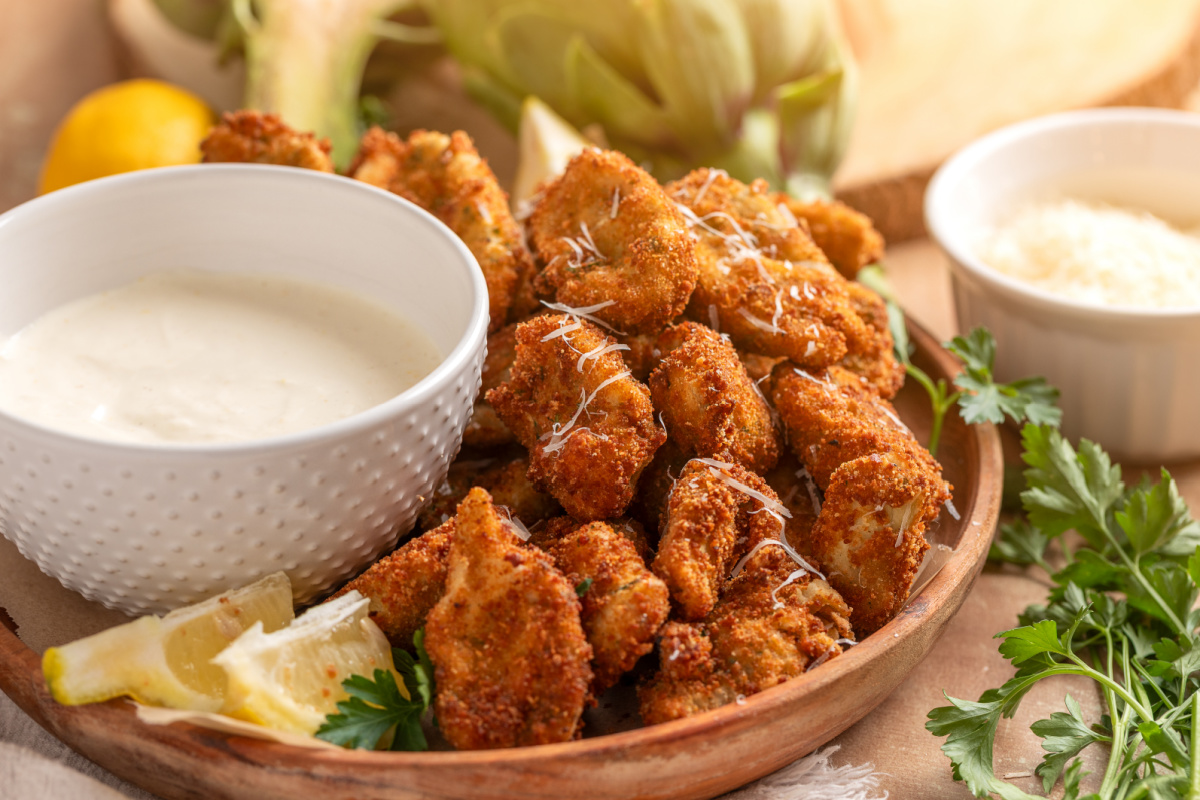 Crispy fried artichokes served with lemon garlic aioli and fresh lemon wedges Fried artichokes with lemon garlic aioli on a wooden platter with lemon wedges and parsley