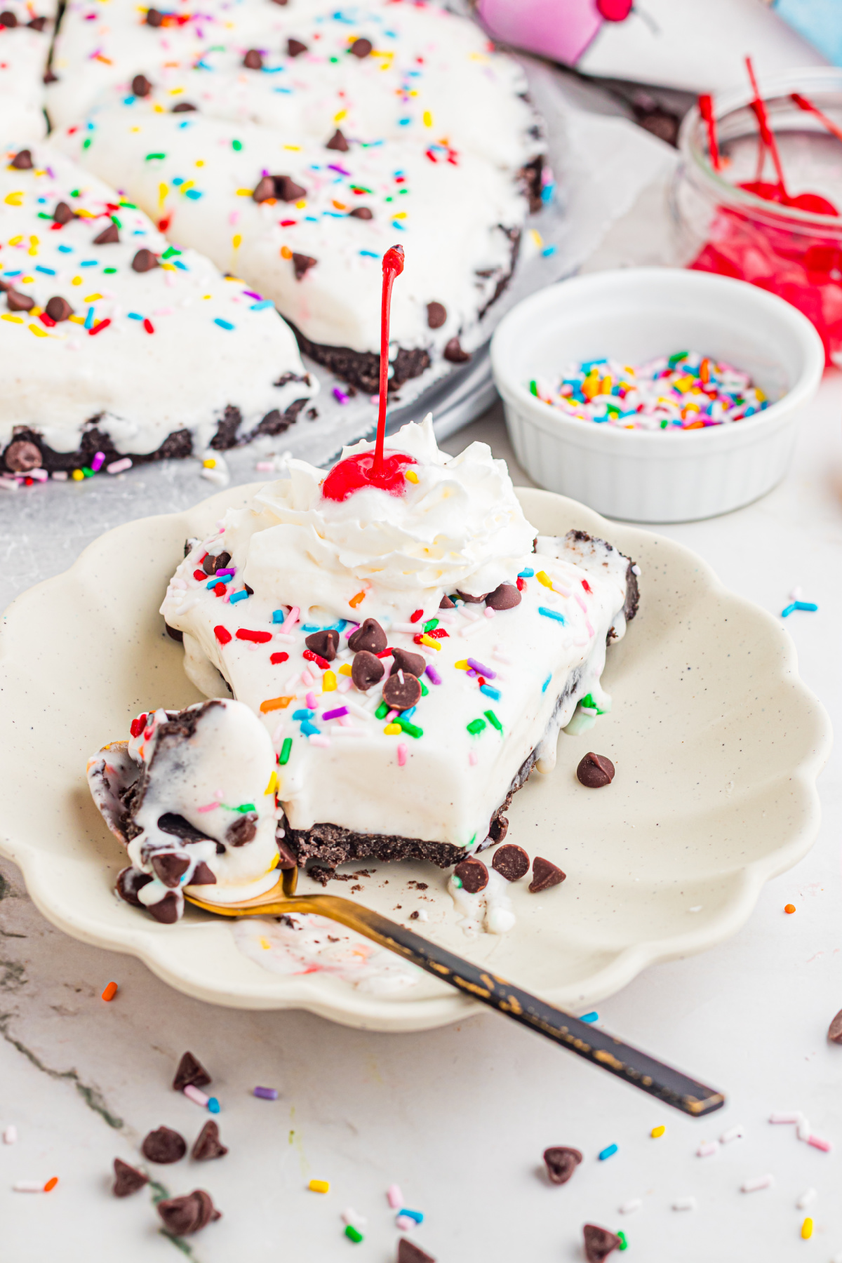 Ice Cream Dessert Pizza Slice with Whipped Cream and Cherry slice of ice cream dessert pizza with Oreo crust topped with whipped cream, cherry, sprinkles, and chocolate chips