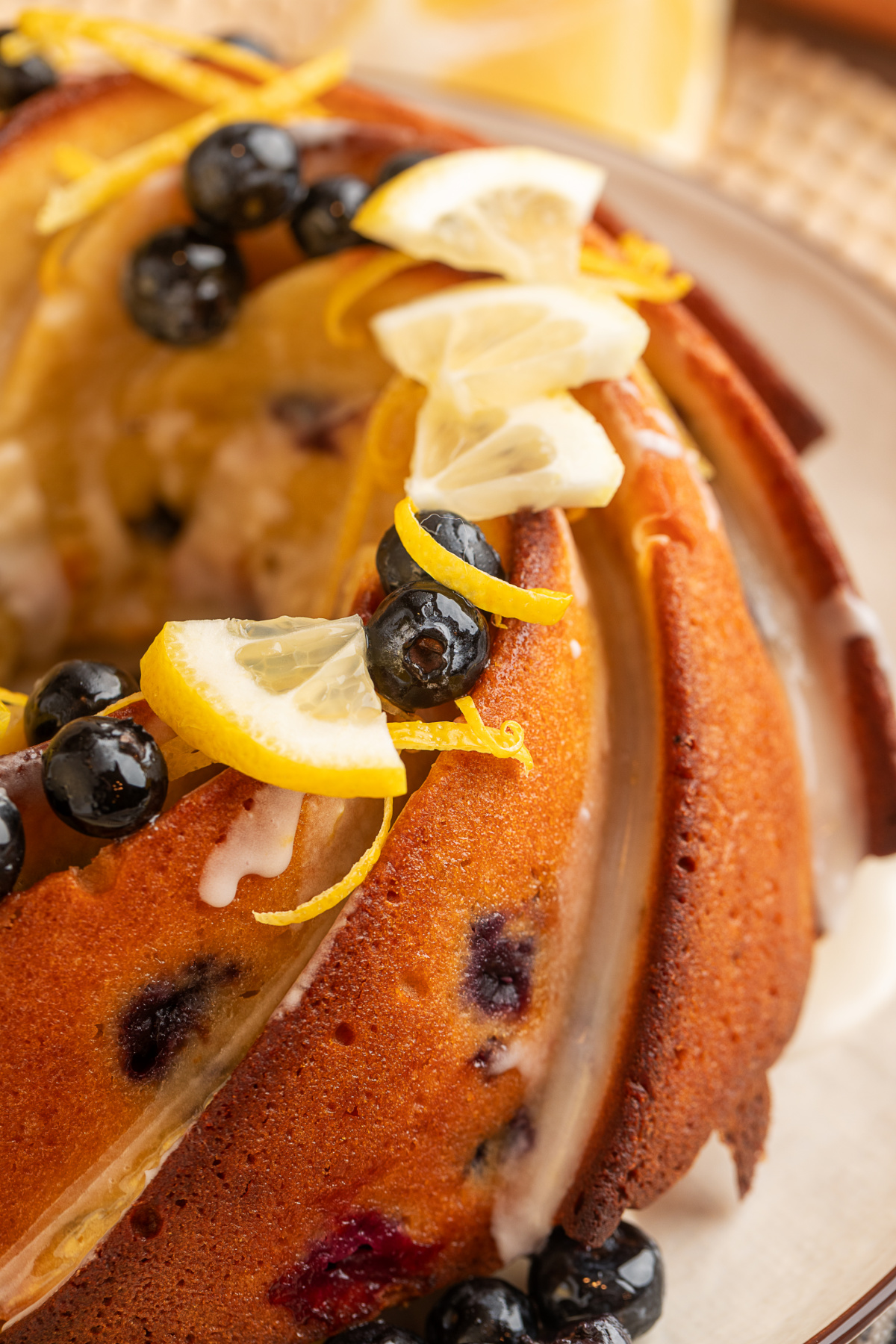 close up of lemon blueberry sour cream bundt cake with glaze lemon blueberry sour cream bundt cake close up with lemon glaze, blueberries, and lemon slices