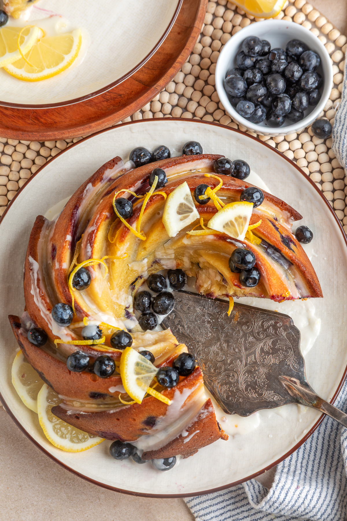 lemon blueberry sour cream bundt cake with slice removed and glaze lemon blueberry sour cream bundt cake sliced on a plate with glaze, fresh blueberries, and lemon slices