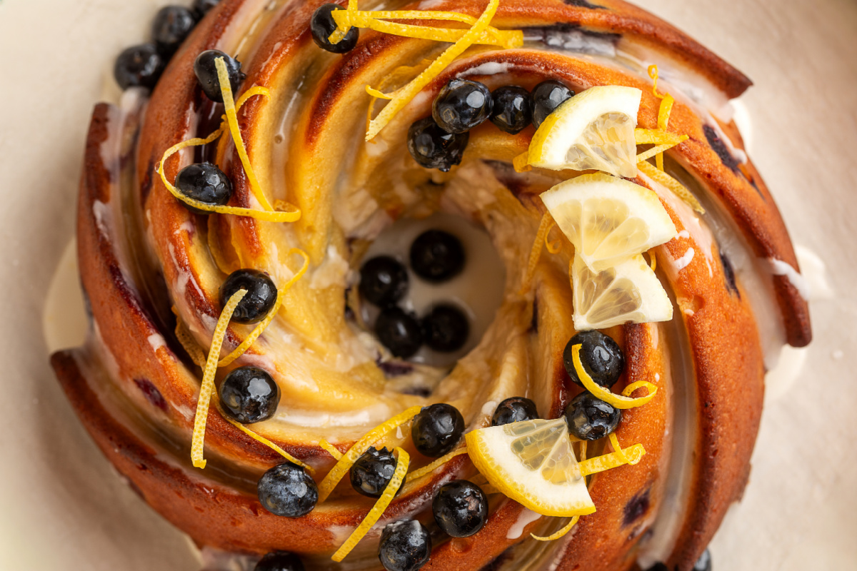 top view of lemon blueberry sour cream bundt cake with glaze lemon blueberry sour cream bundt cake from above with lemon glaze, blueberries, and lemon zest