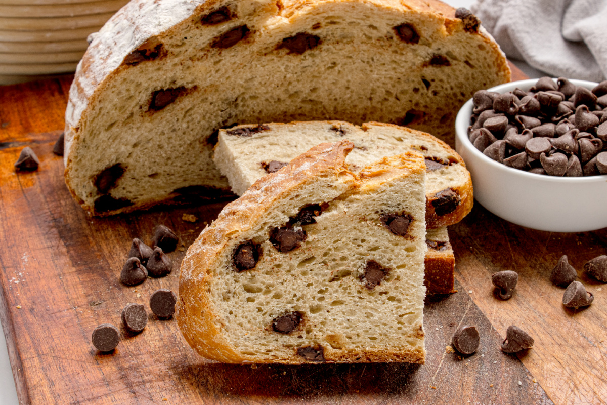 Sliced bread on a cutting board with chocolate chips baked into each piece Chocolate Chip Artisan Bread sliced on a wooden board with visible chocolate chips and crusty exterior