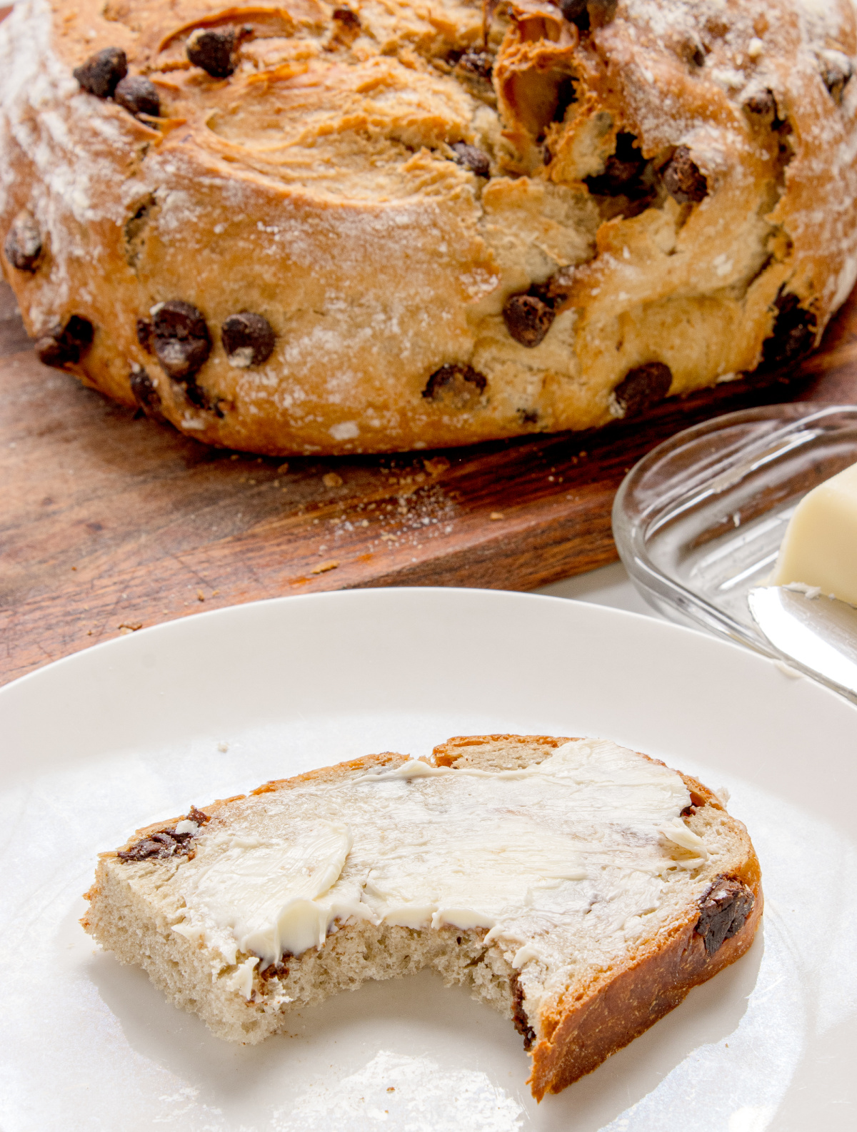 buttered bread slice with a bite showing texture and chocolate pieces slice of chocolate chip bread with butter and a bite taken on a white plate