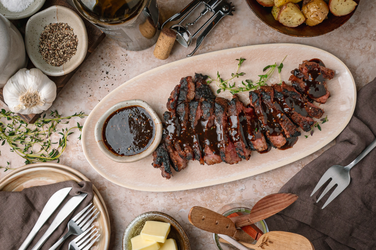 Sliced cocoa rubbed steak served with dark stout pan sauce. Cocoa rubbed steak with dark stout pan sauce sliced on a serving platter with extra sauce on the side.