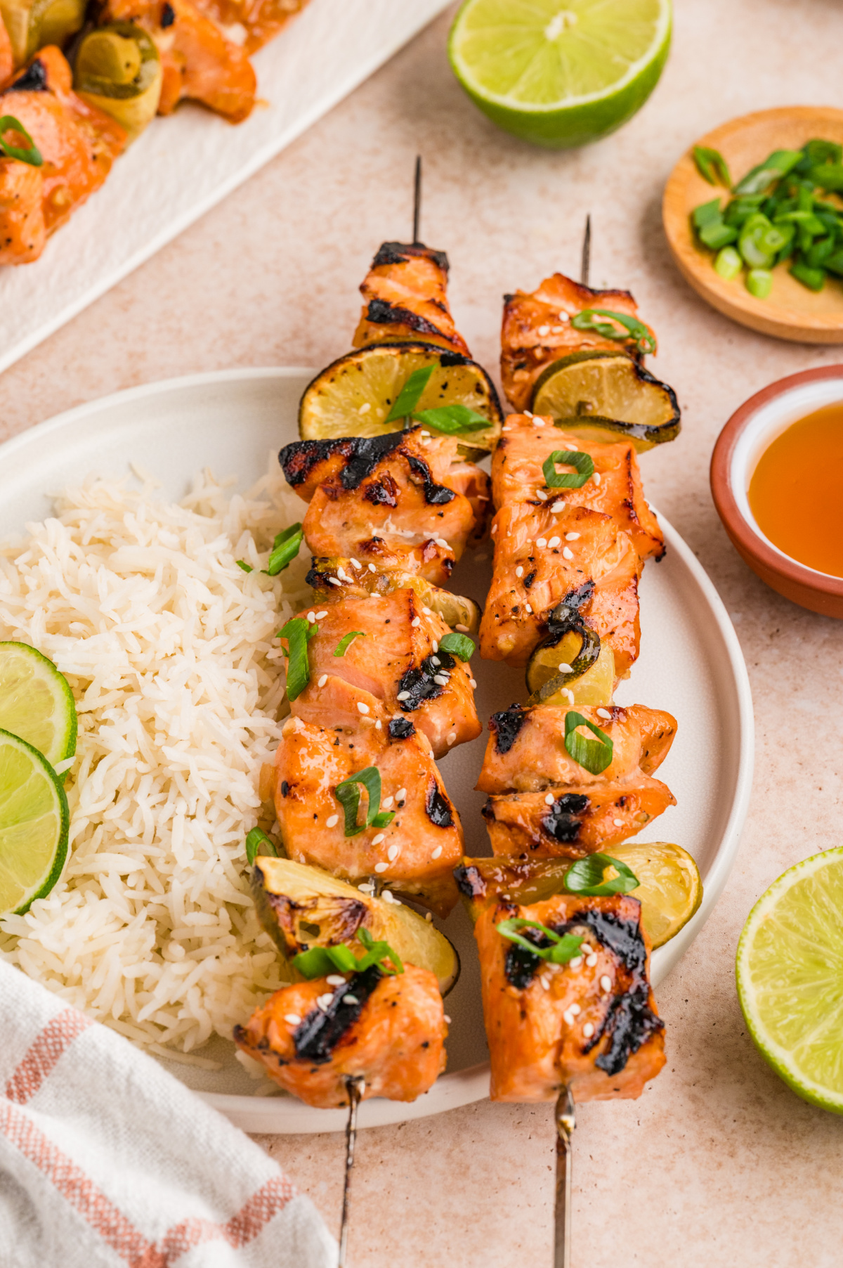 Grilled honey soy lime salmon skewers served with white rice, charred lime slices, sesame seeds, and green onions on a dinner plate.