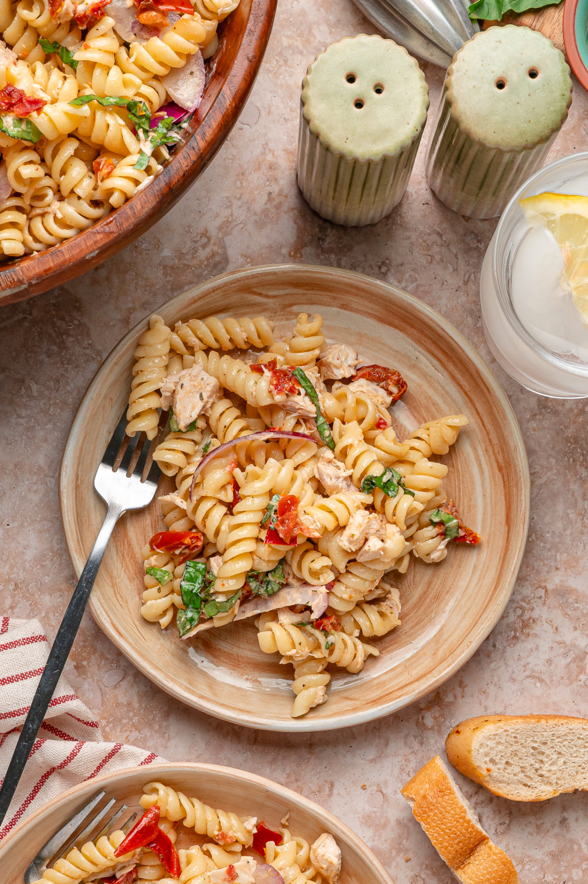 Chicken pasta salad served on plates with basil, rotini, sun-dried tomatoes, and a light Parmesan dressing Plates of Sun-Dried Tomato Chicken Pasta Salad with rotini, basil, chicken, red onion, and chopped sun-dried tomatoes